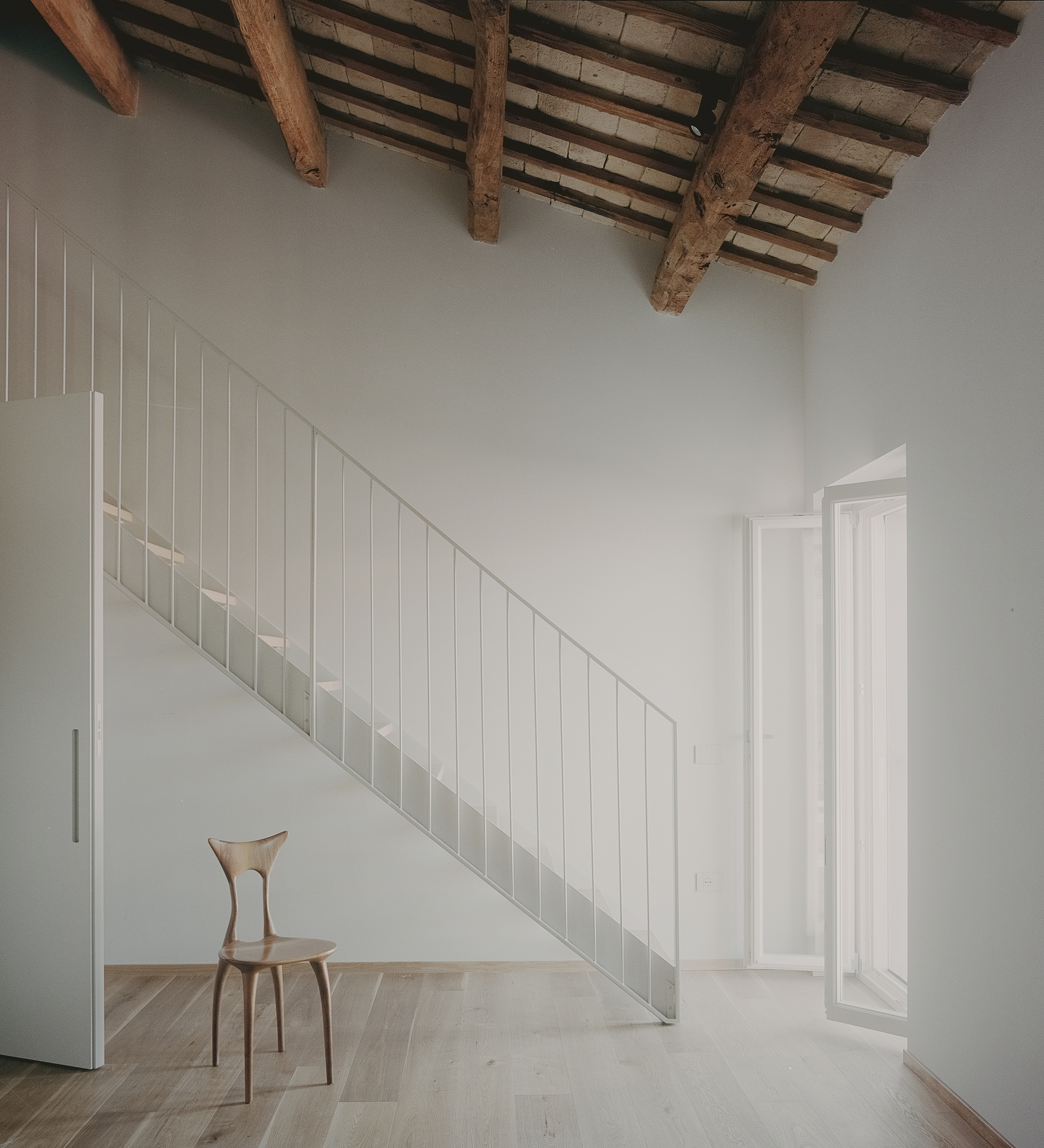 Interior staircase beneath exposed timber beams and terracotta tile ceiling with diffused natural light