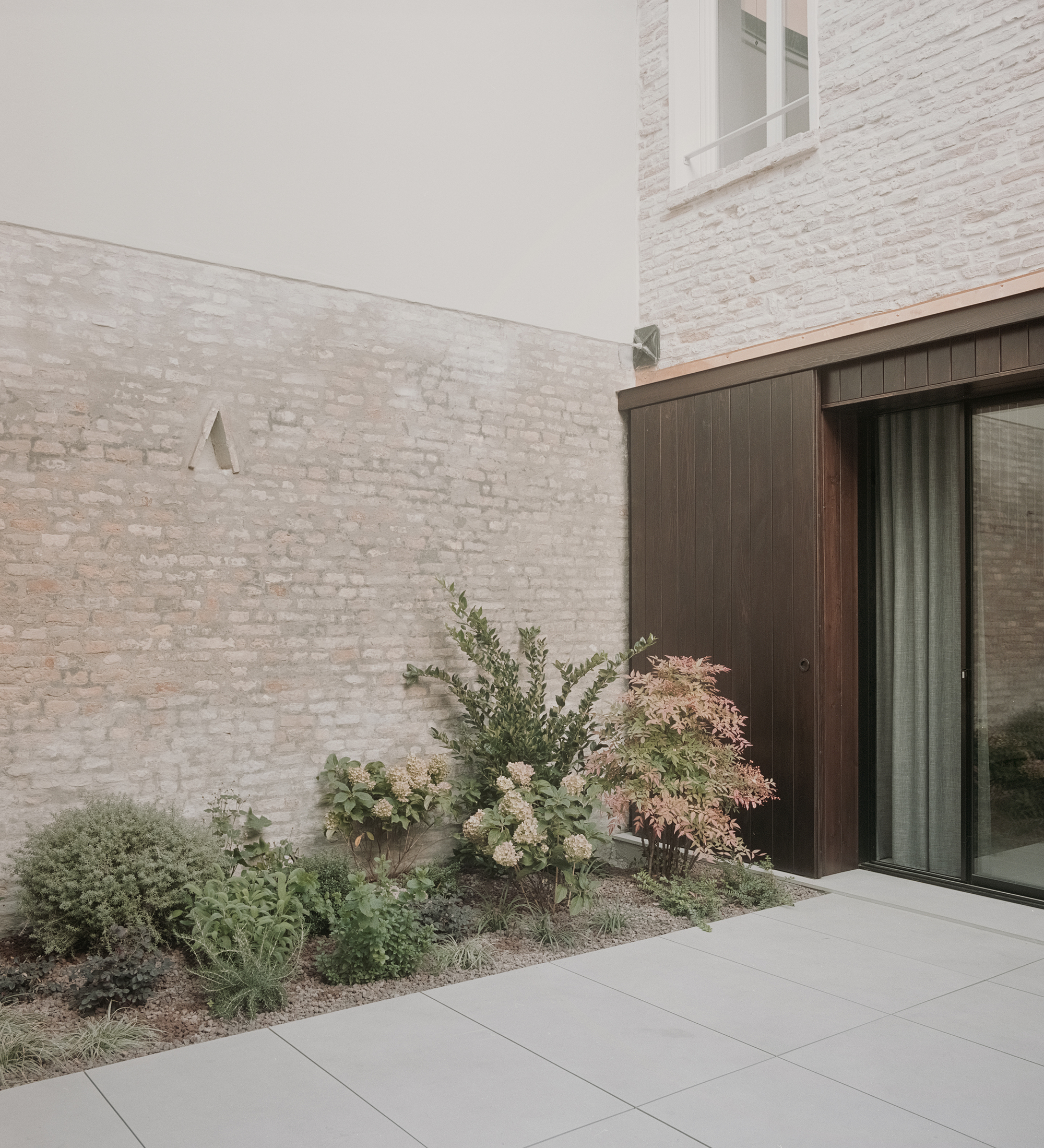 Whitewashed brick courtyard wall with a planted bed beside vertical timber cladding and sliding glass door
