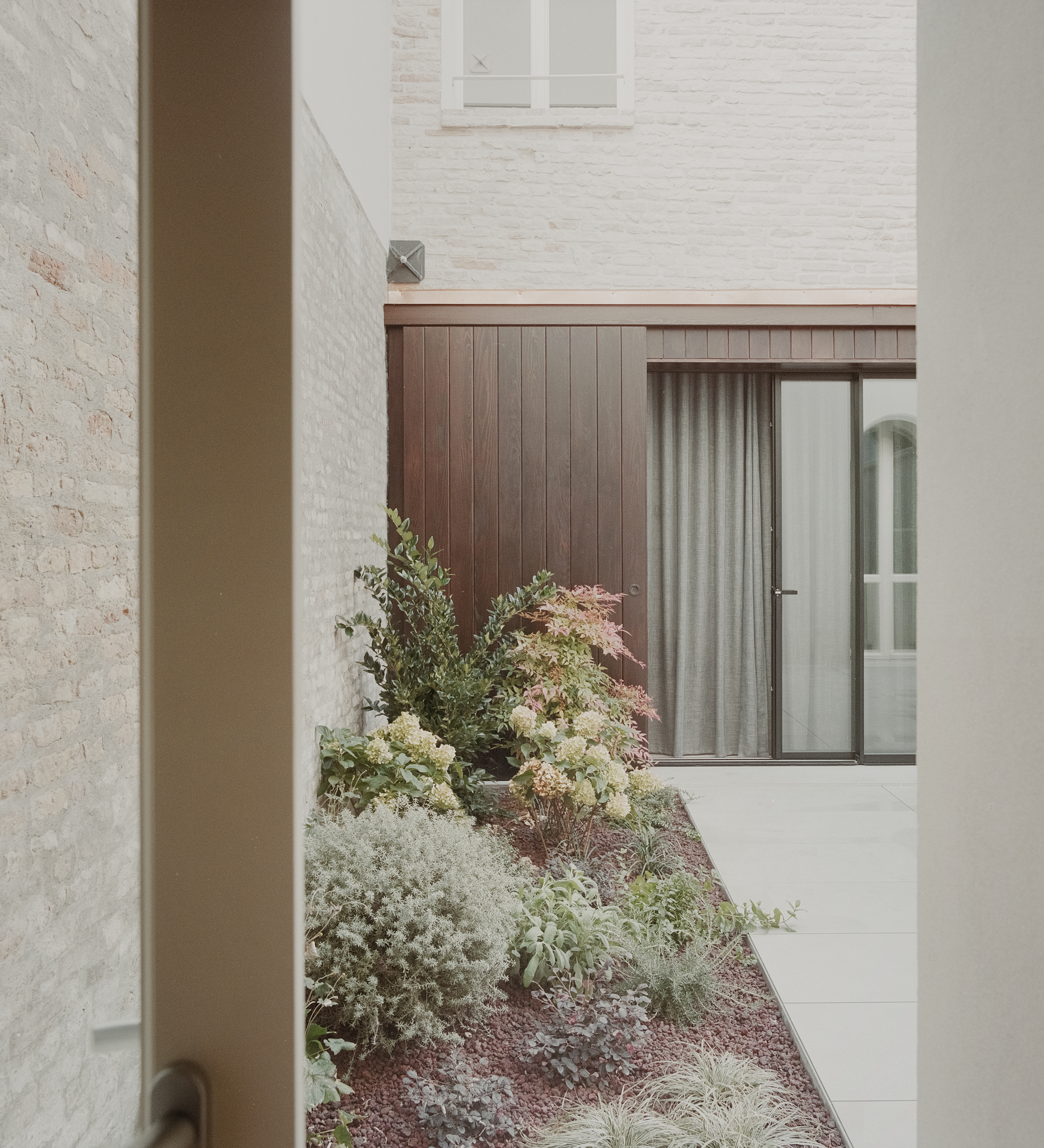 Narrow courtyard passage framed by painted brick walls with low plantings along the paved floor