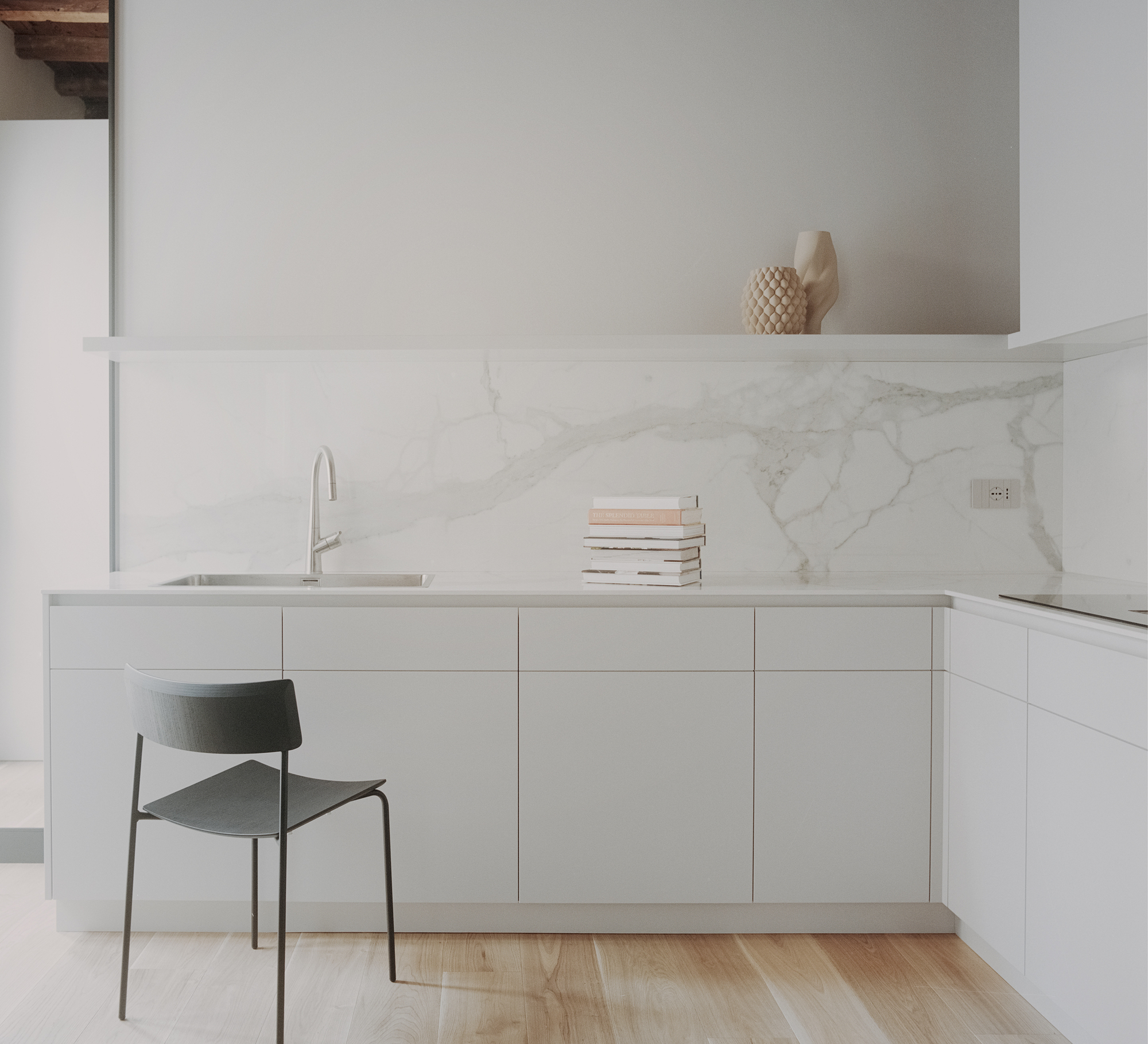 Kitchen counter with white marble backsplash and a single chair on pale wooden flooring
