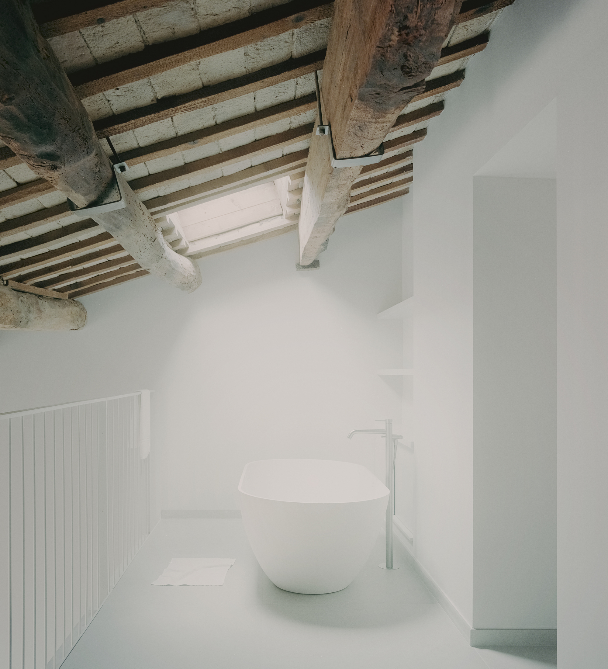 Bathroom with freestanding white tub beneath exposed timber beams and a skylight above