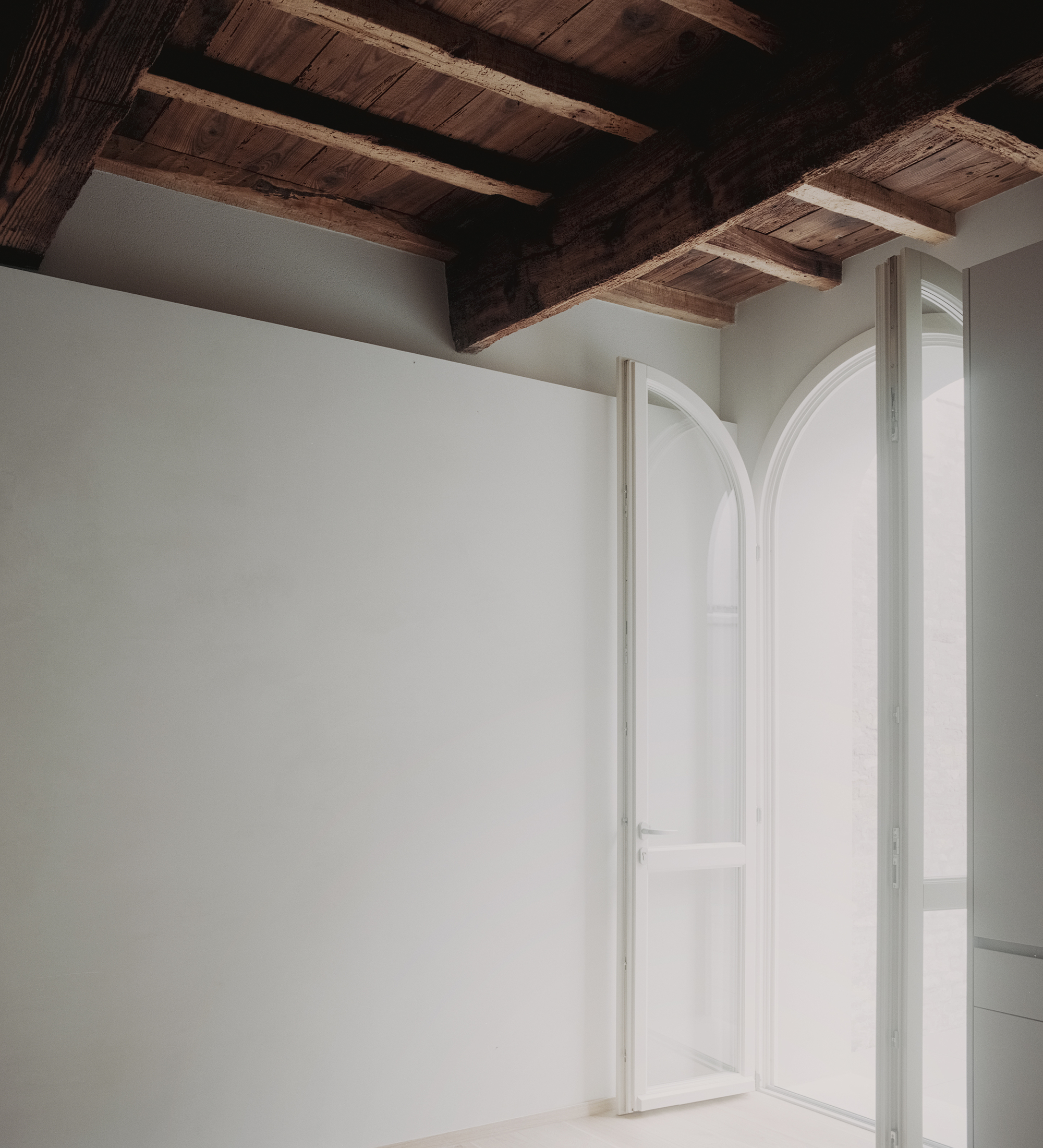 Arched double doors opening to bright space under dark timber beam and plank ceiling