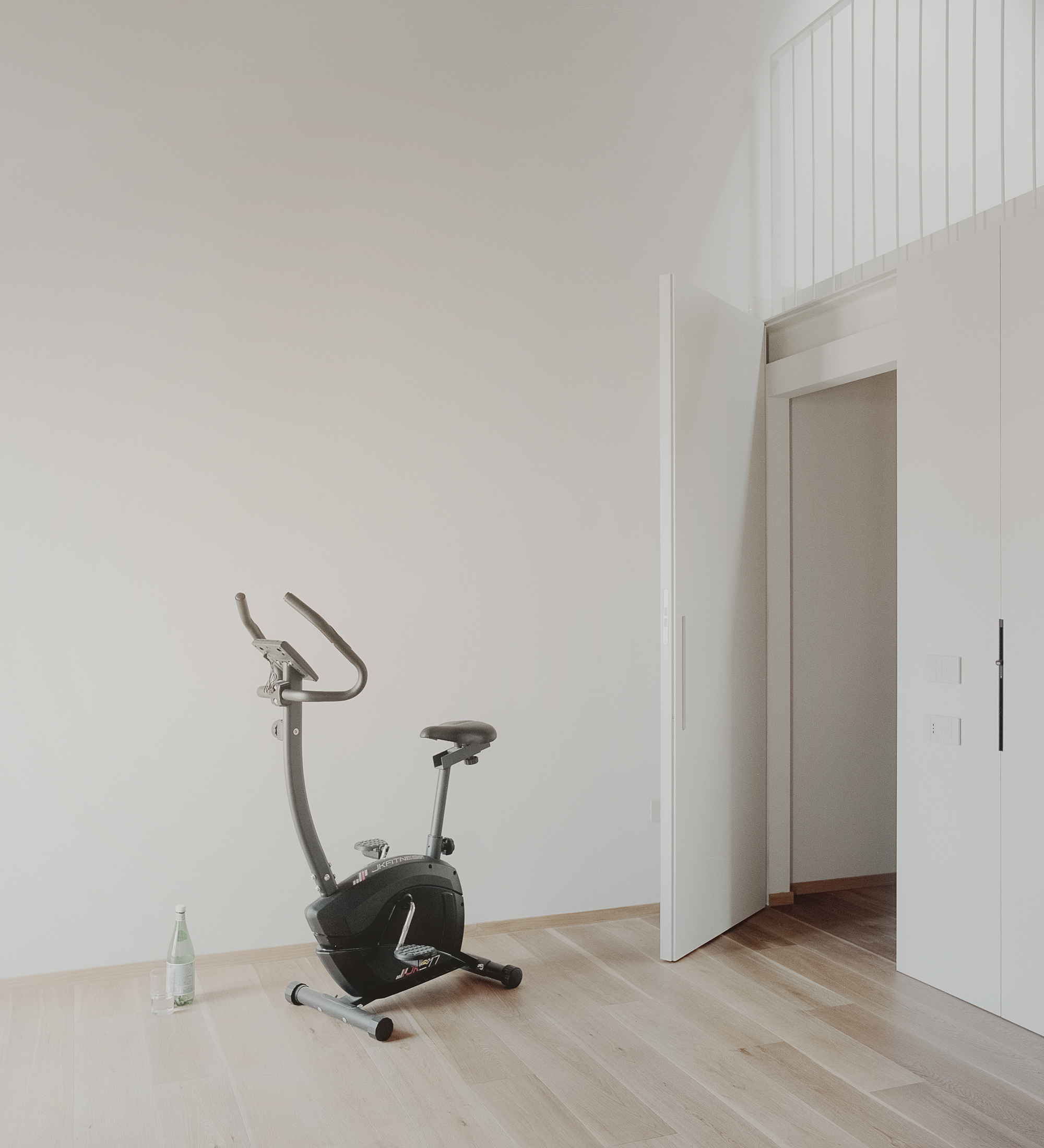 White-walled room with an exercise bike on light wood flooring near a doorway opening