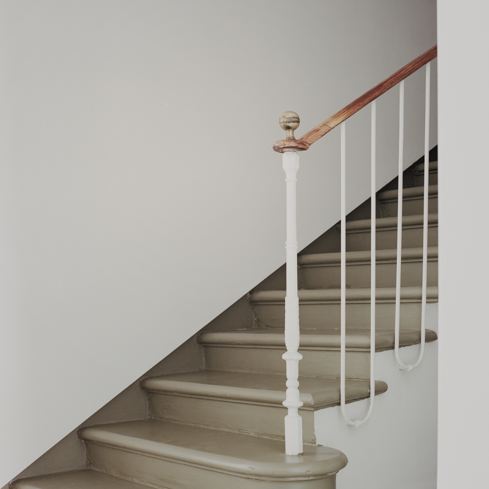 Curved staircase with turned white newel post and minimal steel rod railing ascending upward