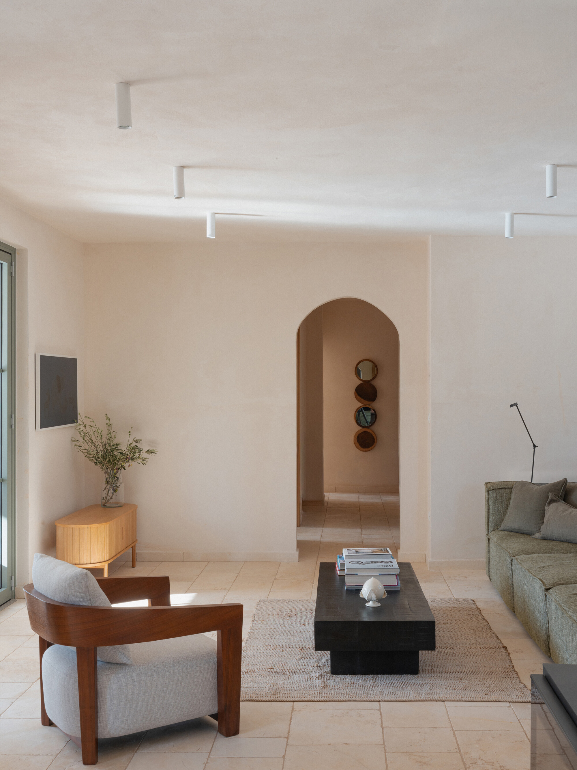 Living room with arched passage and square-profile pendant lights casting afternoon sun across limestone tile floor