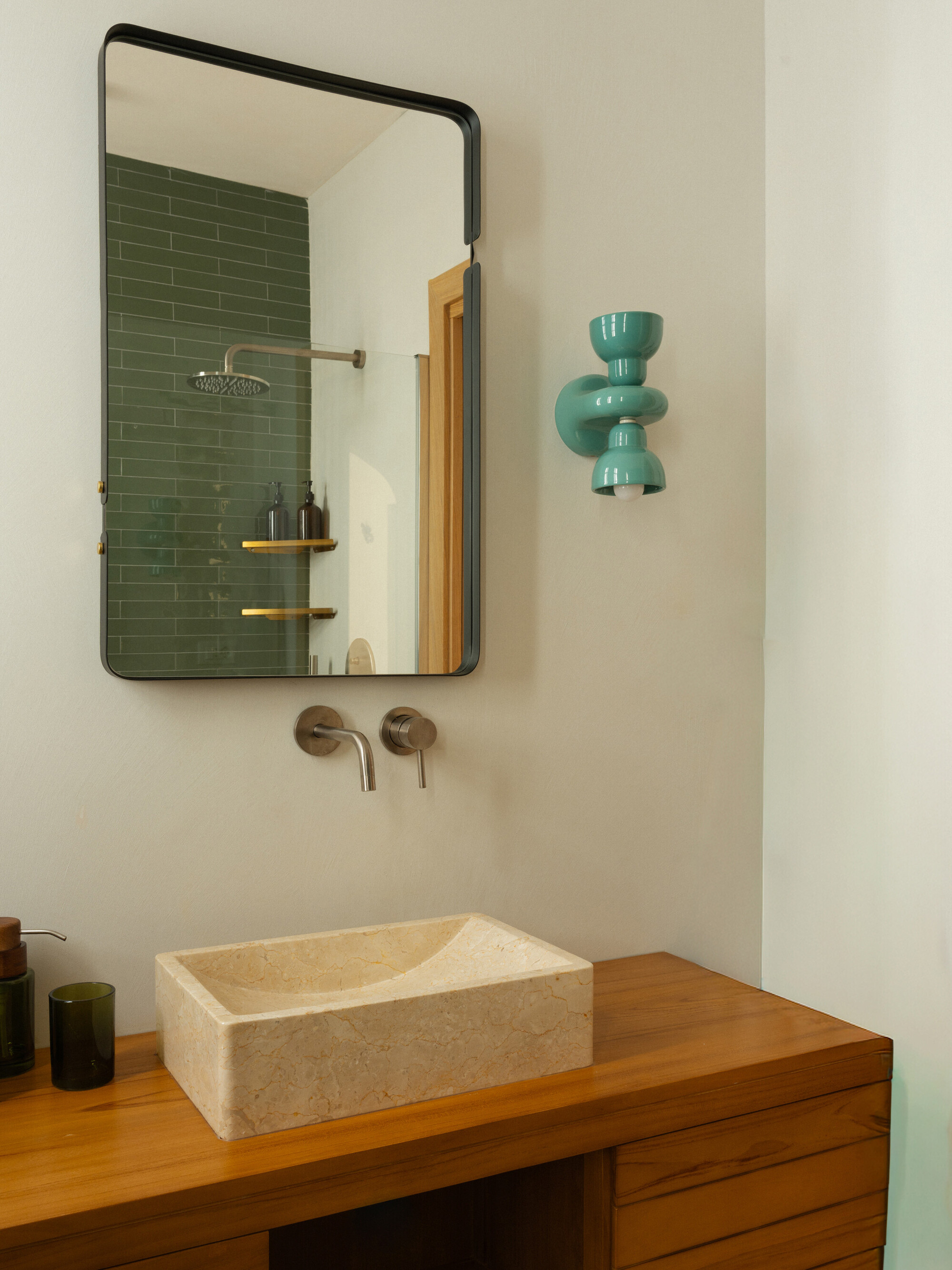 Bathroom vanity with limestone vessel sink on timber cabinet, mirror reflecting green subway tile shower
