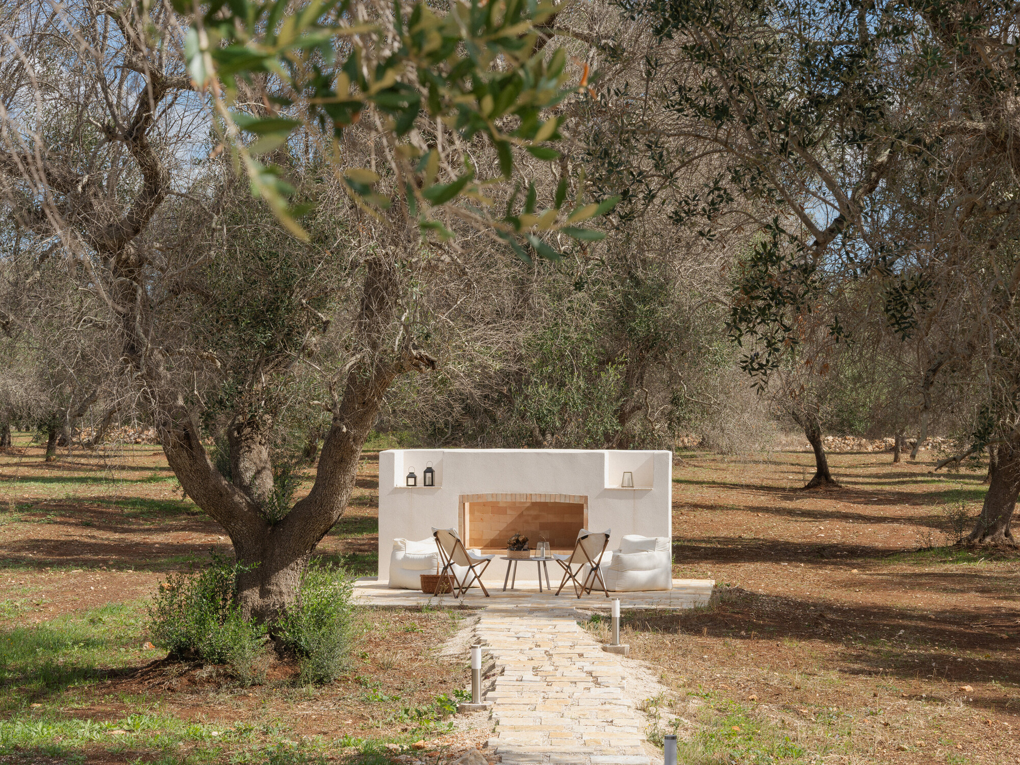 Freestanding white outdoor kitchen with arched opening in an olive grove under scattered clouds