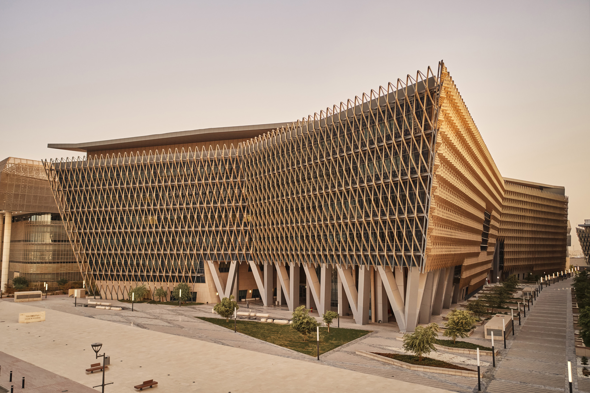 Corner view of the parametric timber lattice facade supported by angular concrete columns in afternoon light