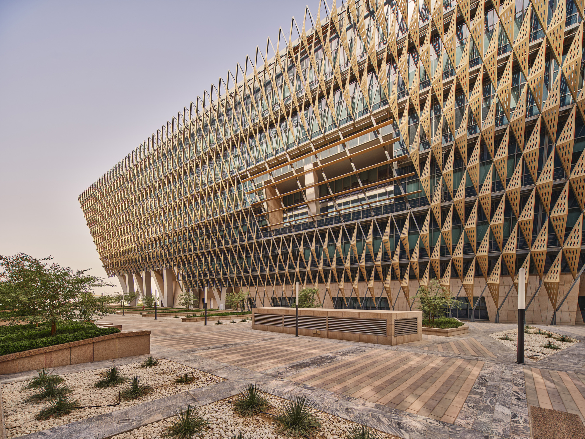 Ground-level view of the lattice facade with carved aperture above the landscaped entrance plaza