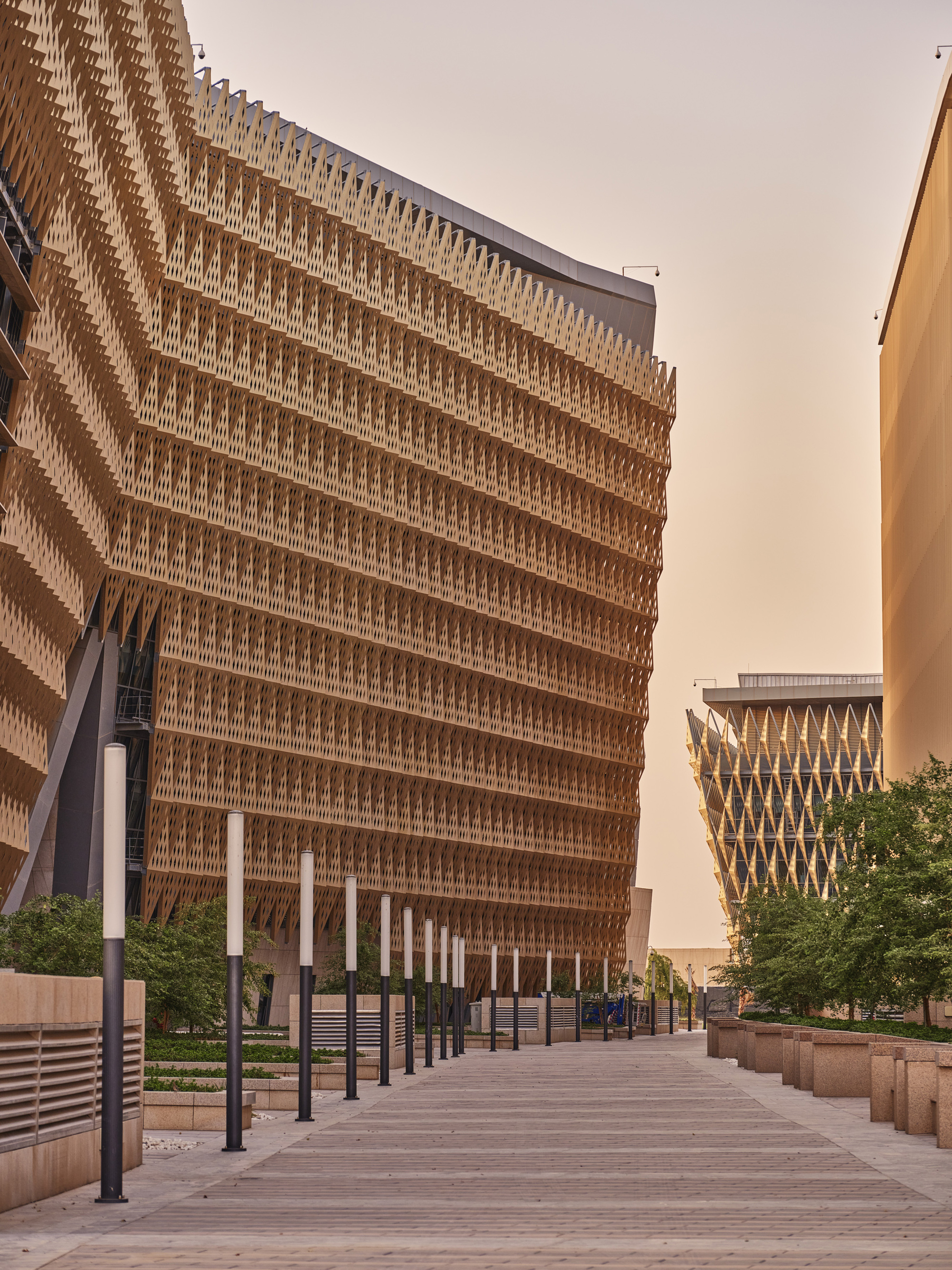 Pedestrian pathway flanked by buildings with patterned timber brise-soleil facades under an overcast sky