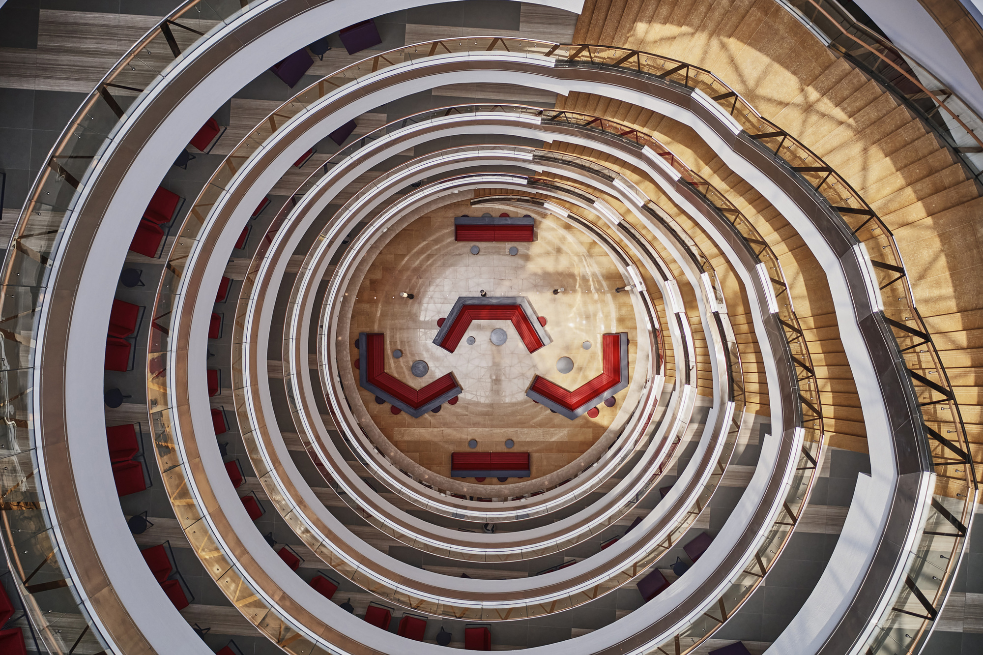 Overhead view of concentric atrium balconies surrounding hexagonal ground floor with red furniture