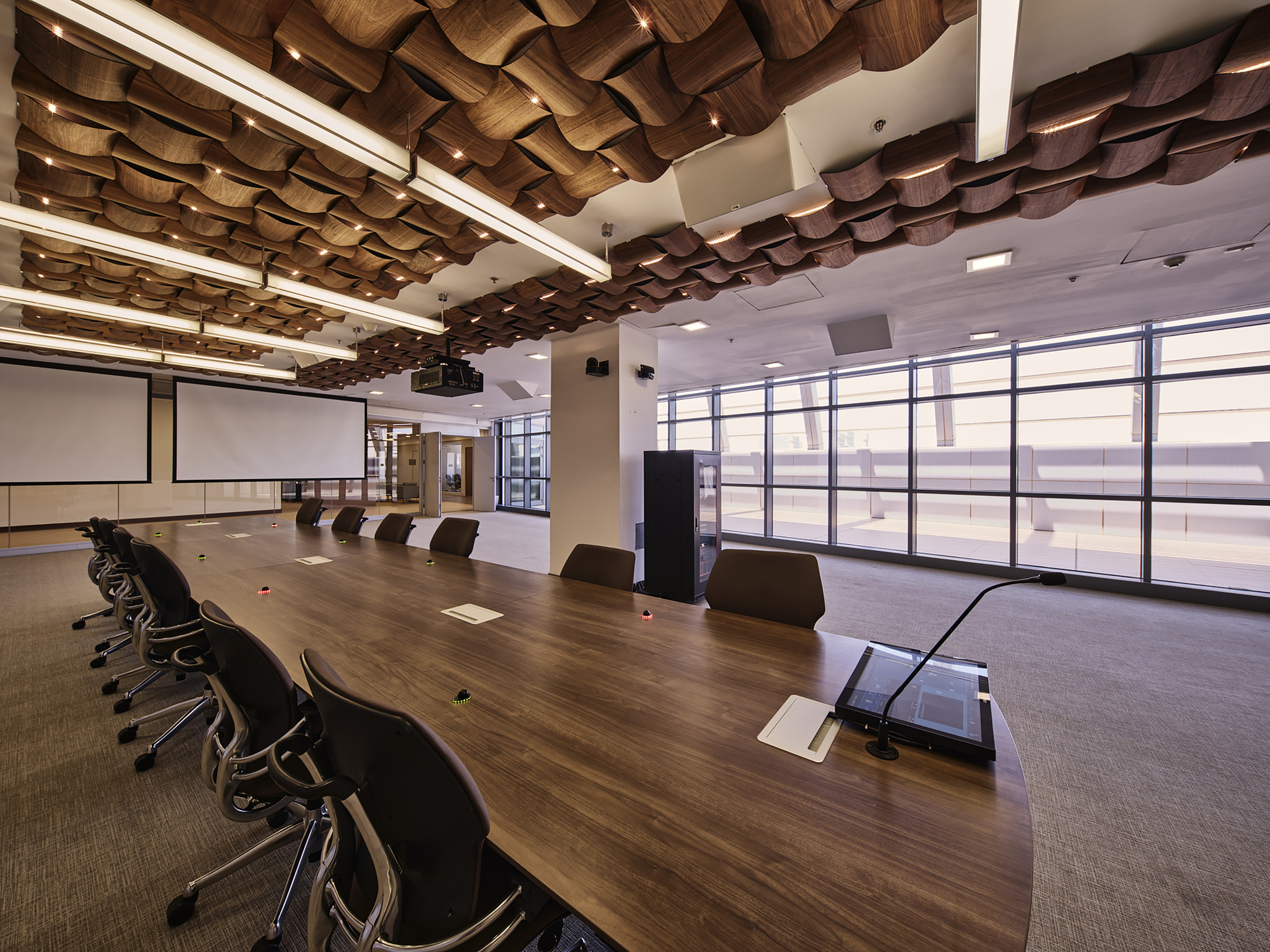 Conference room with long timber table and sculptural woven ceiling panels above glass curtain wall