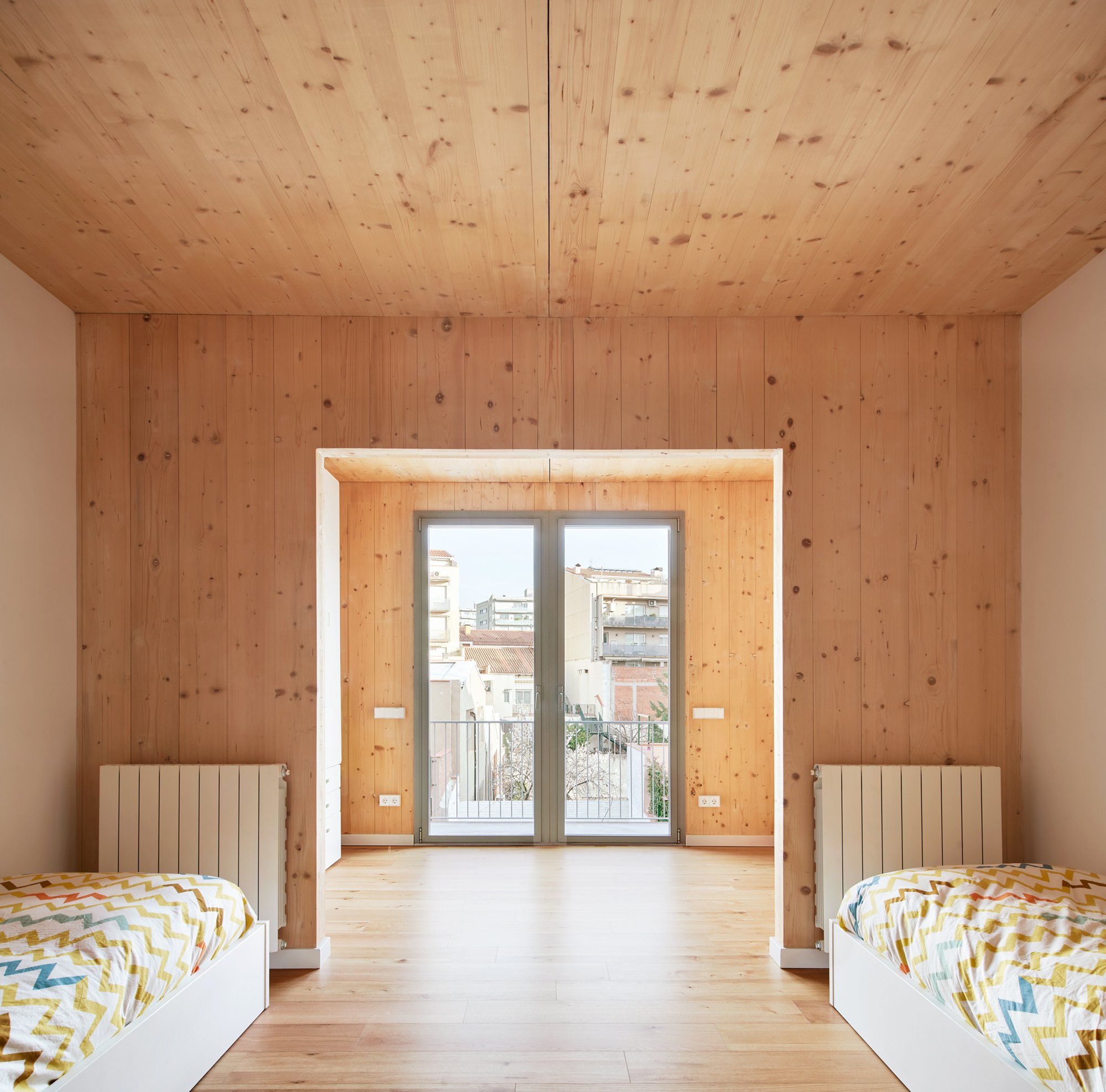 Bedroom with twin beds flanking deep timber-lined window opening with radiators and balcony access