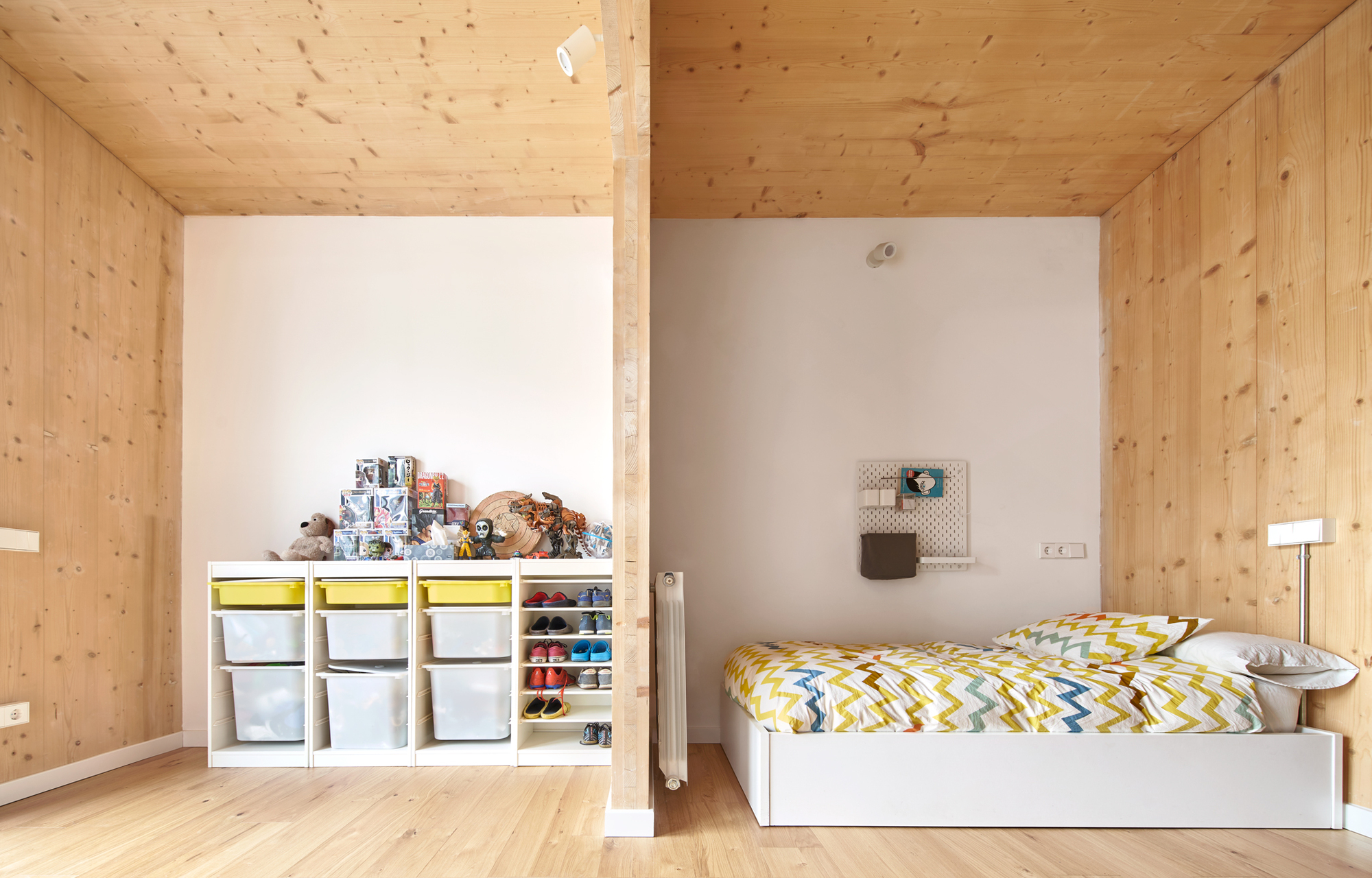 Corner of bedroom showing pine ceiling and walls with toy storage beside single bed