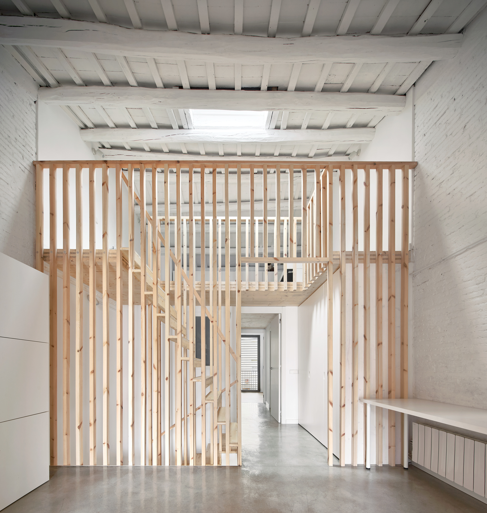 Double-height space with timber slat screen enclosing staircase beneath exposed joists and skylight