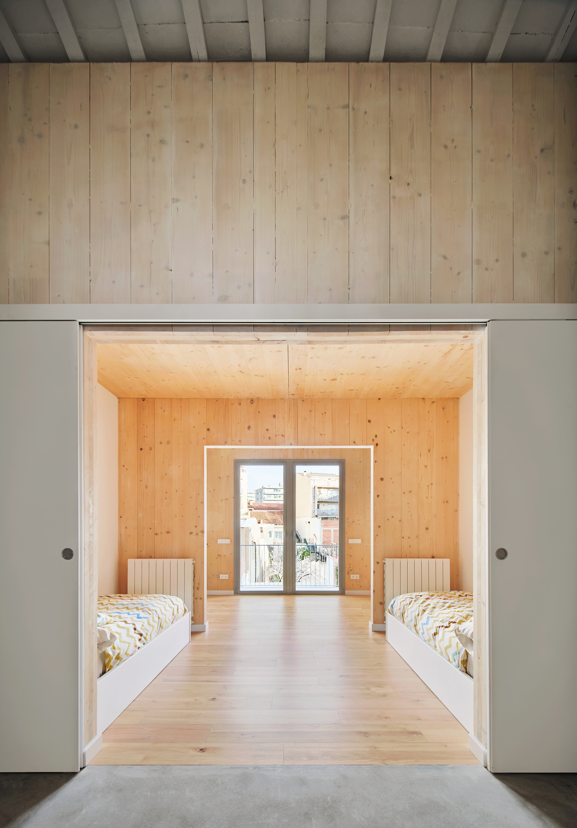 View through a framed doorway into a bedroom with two beds flanking a central window