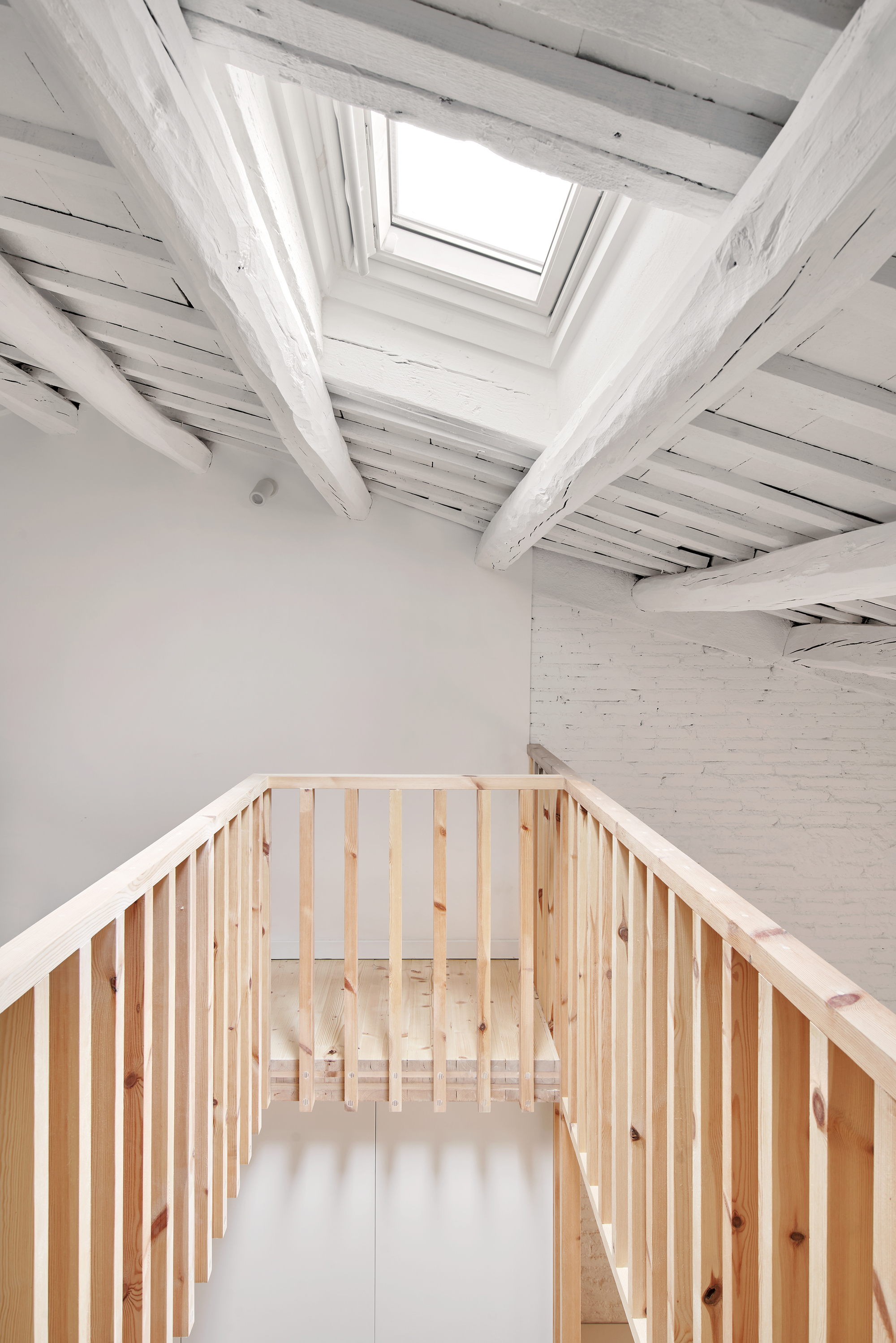 Looking up at timber slatted balustrade and whitewashed ceiling beams with central skylight above