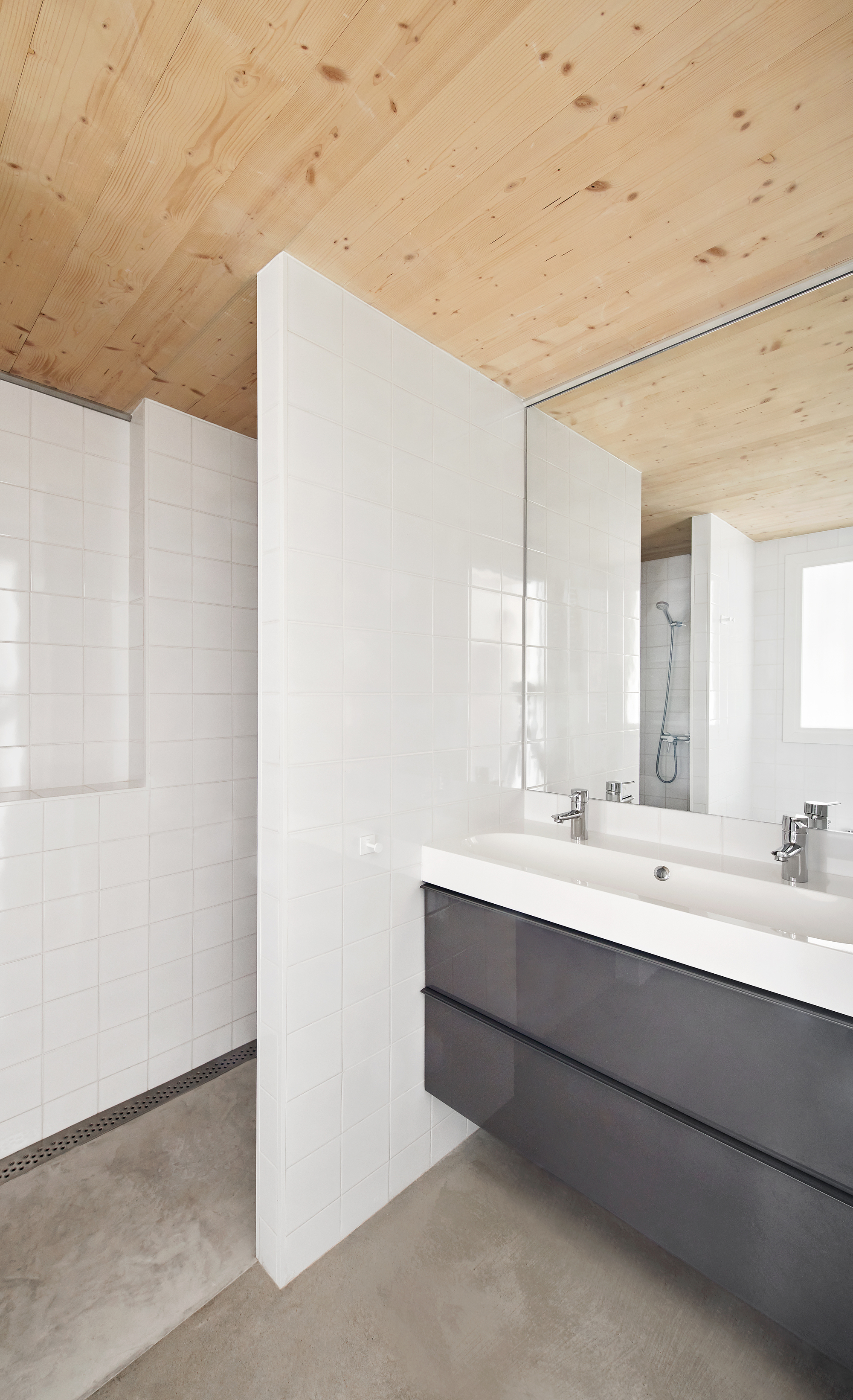 Bathroom with white tile walls, double vanity and plywood ceiling above polished concrete floor