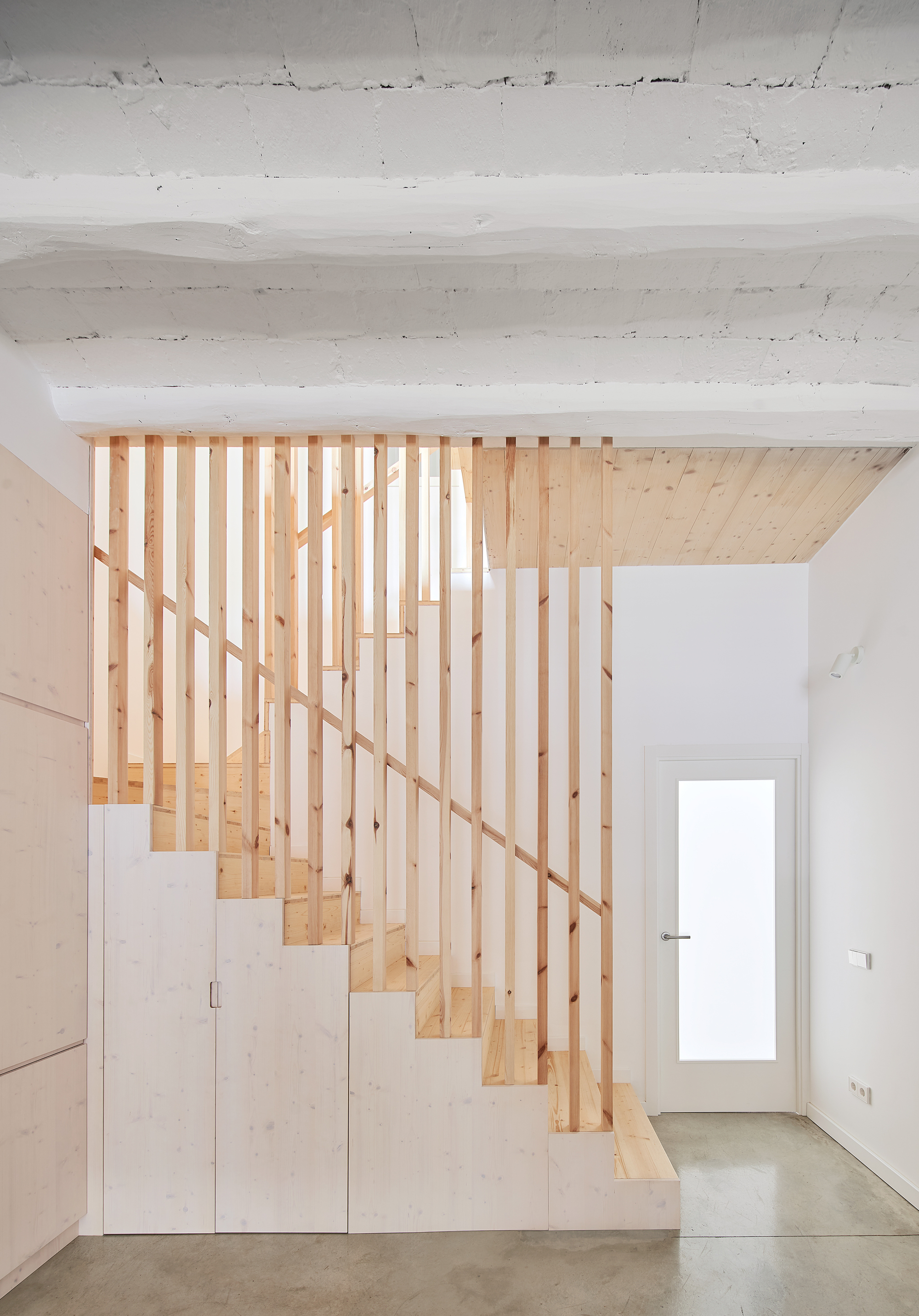 Timber staircase with vertical slat balustrade and plywood storage cabinets beneath the treads