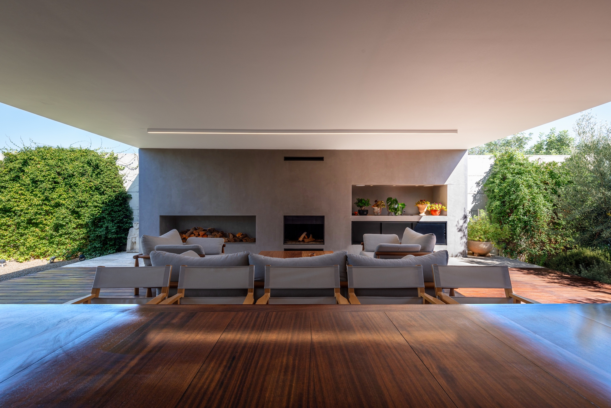 Covered terrace with timber decking, seating, and fireplace wall opening to garden at dusk