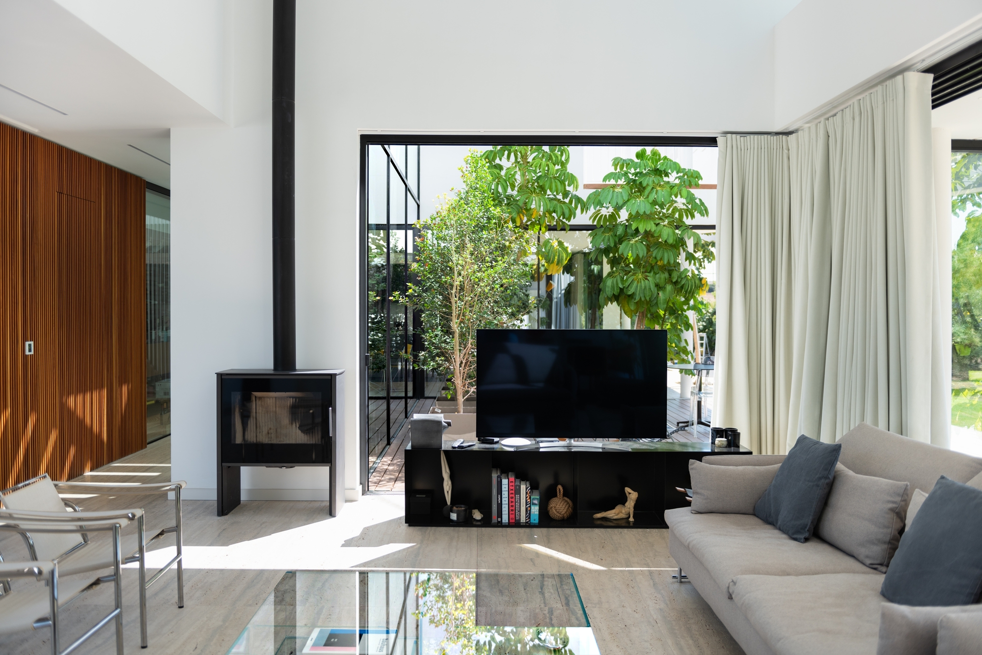 Living room interior with freestanding wood-burning stove and steel-framed glazing overlooking a planted courtyard