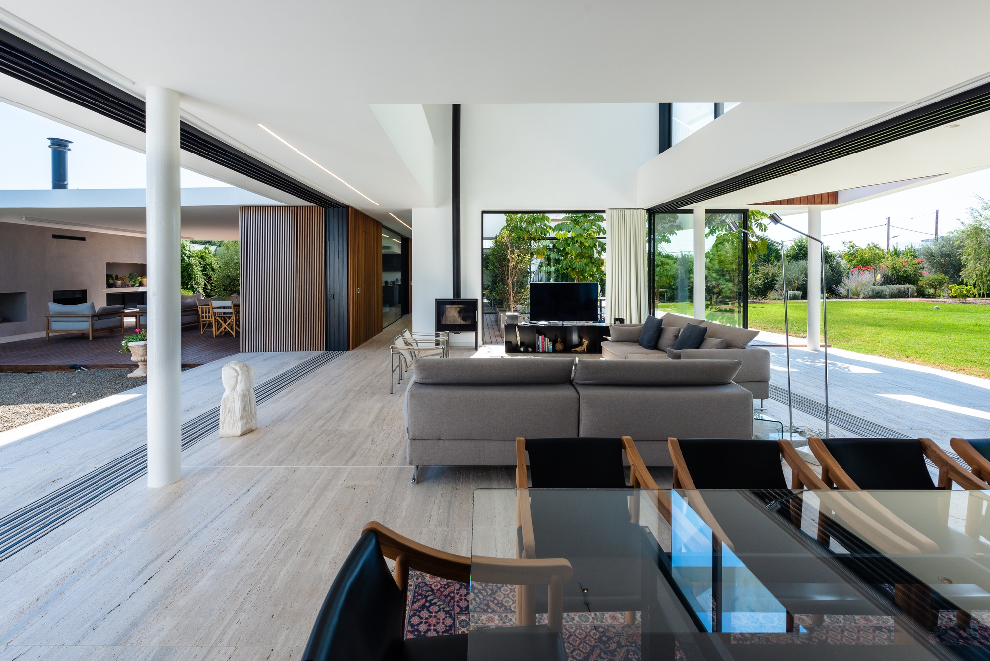 Open-plan living space with white columns and glass thresholds connecting to lawn and courtyard beyond