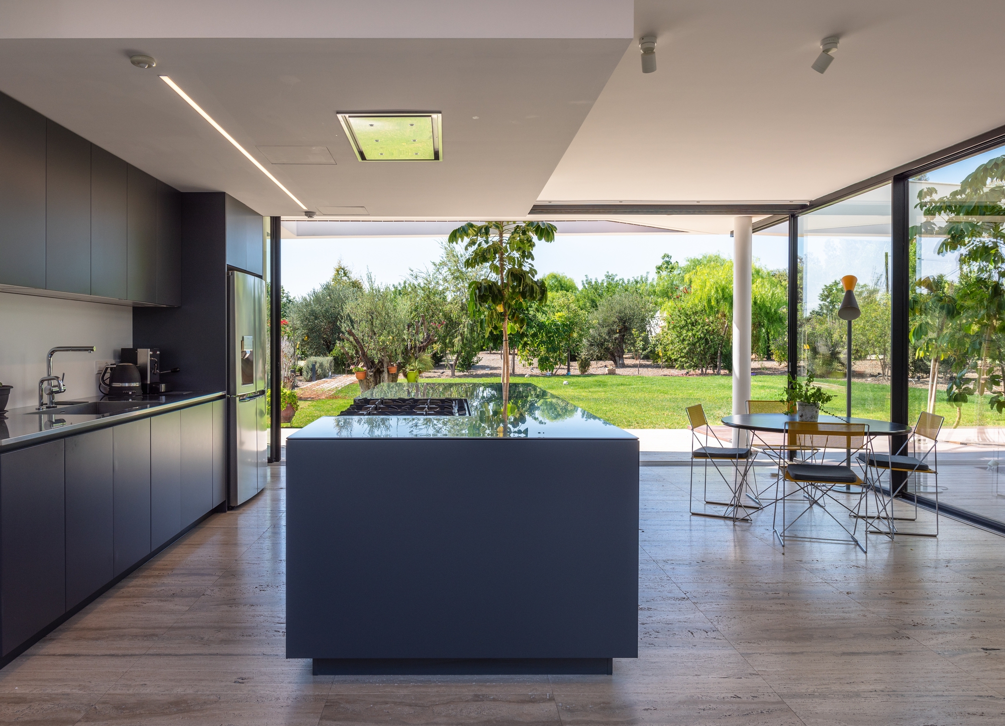 Open-plan kitchen with dark cabinetry and island looking out to lawn through full-height glazing