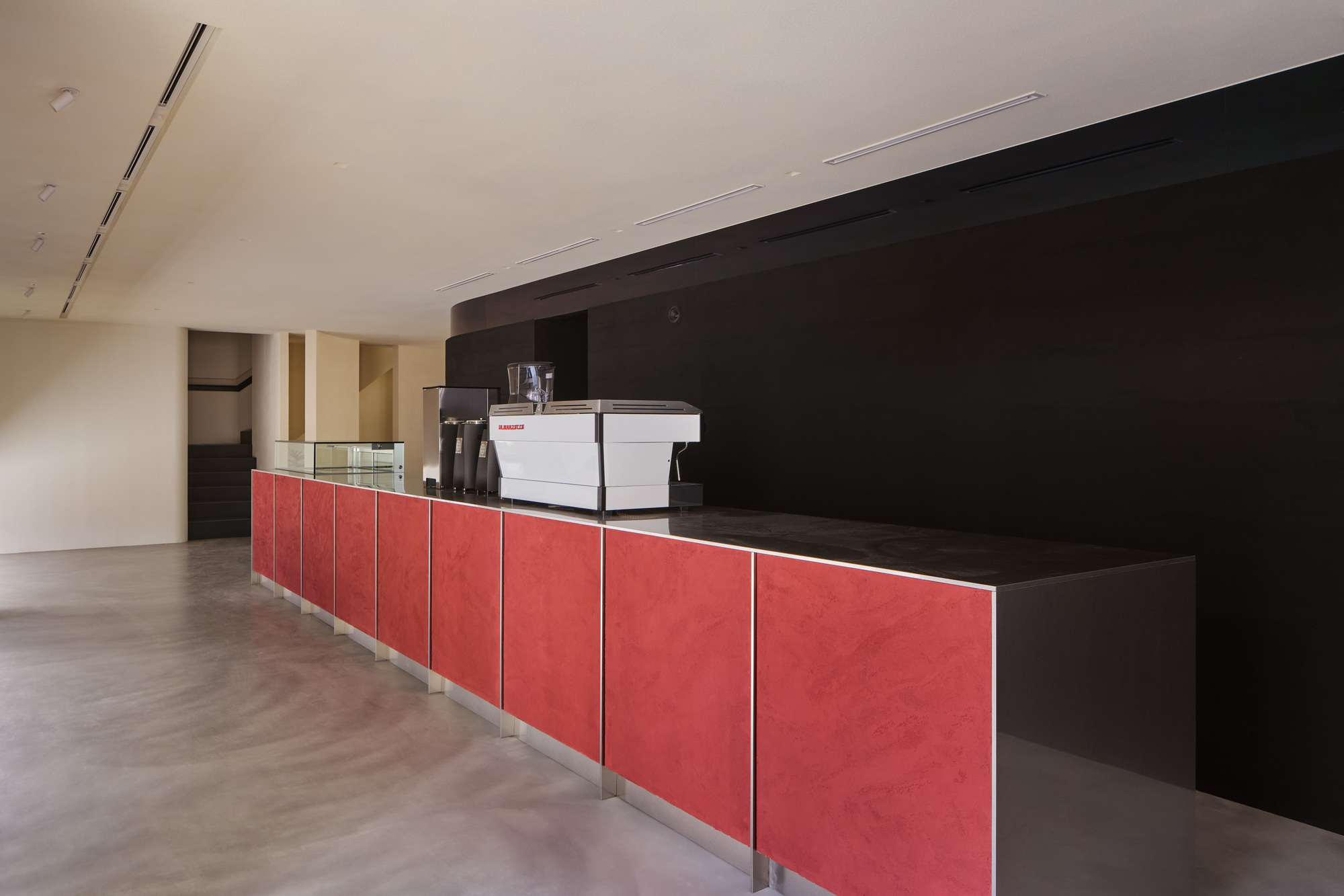 Long service counter with red paneling and black countertop beneath a white vaulted ceiling