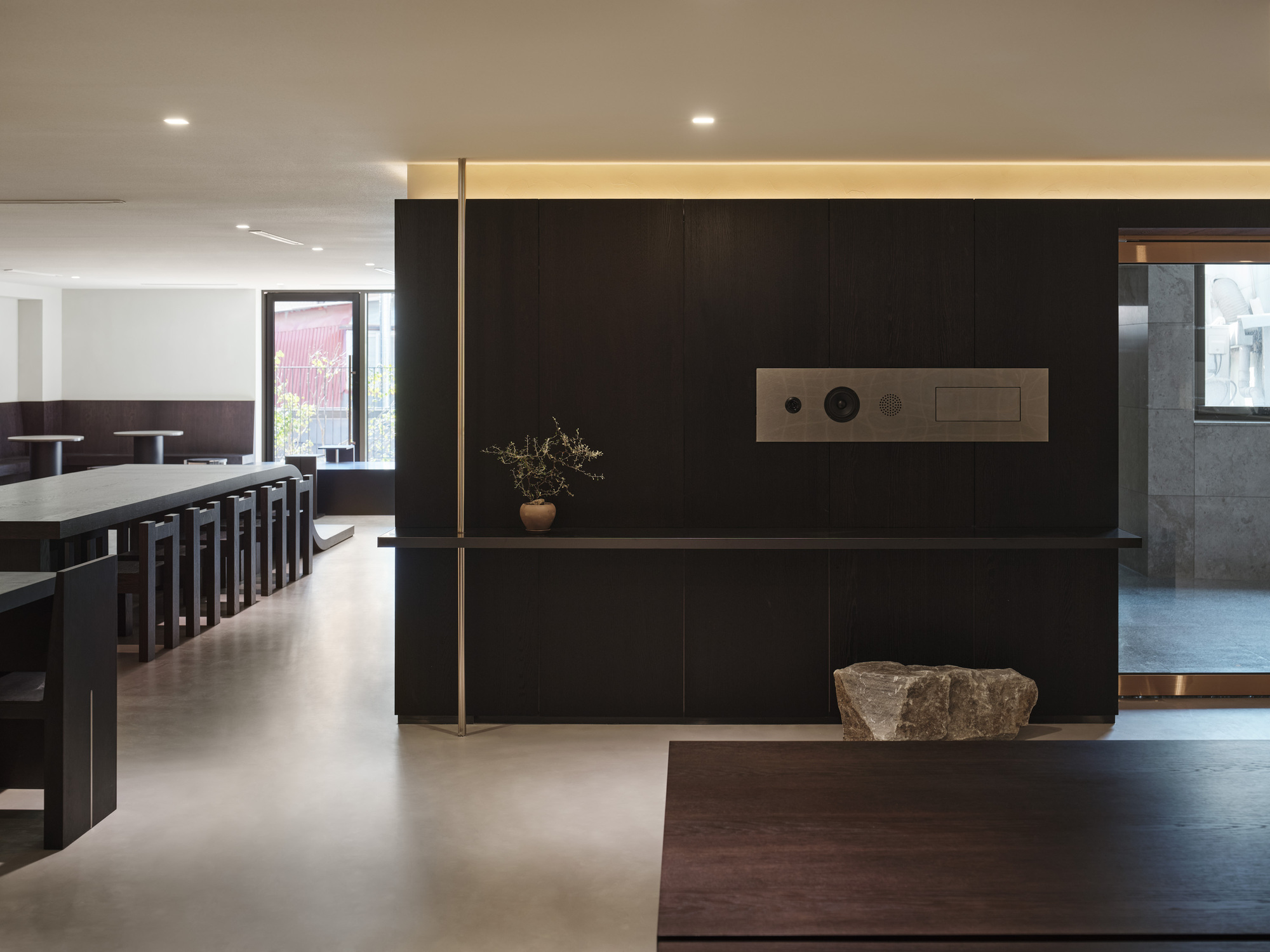 Black panel wall with integrated controls and a raw stone placed at its base