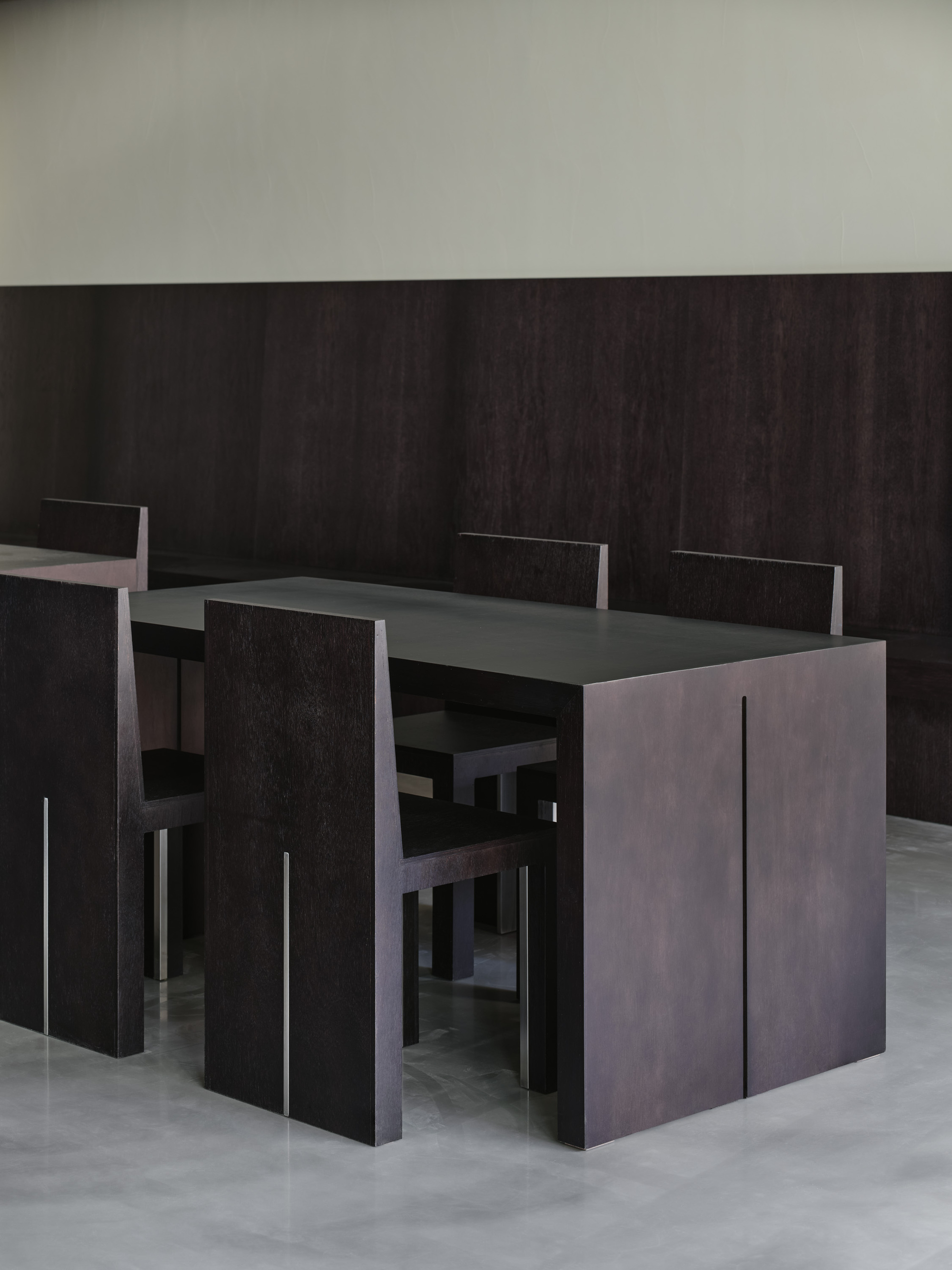 Close-up of black wood table and chairs against a dark paneled wall in even light