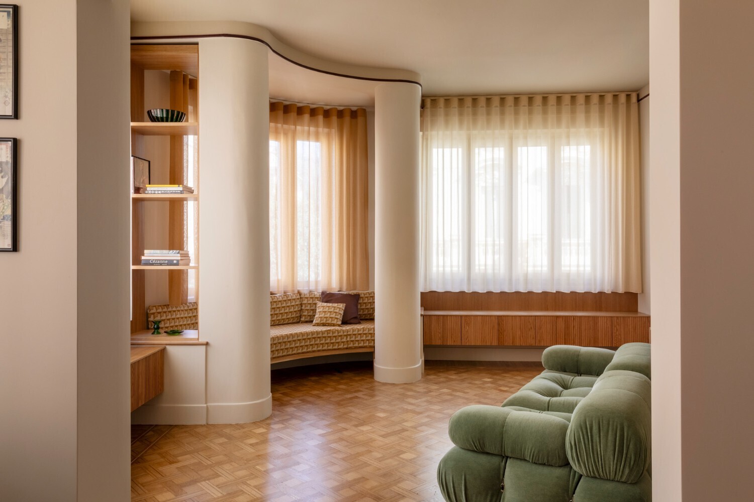 Curved white columns framing built-in timber shelving and a window seat with sheer curtains filtering daylight