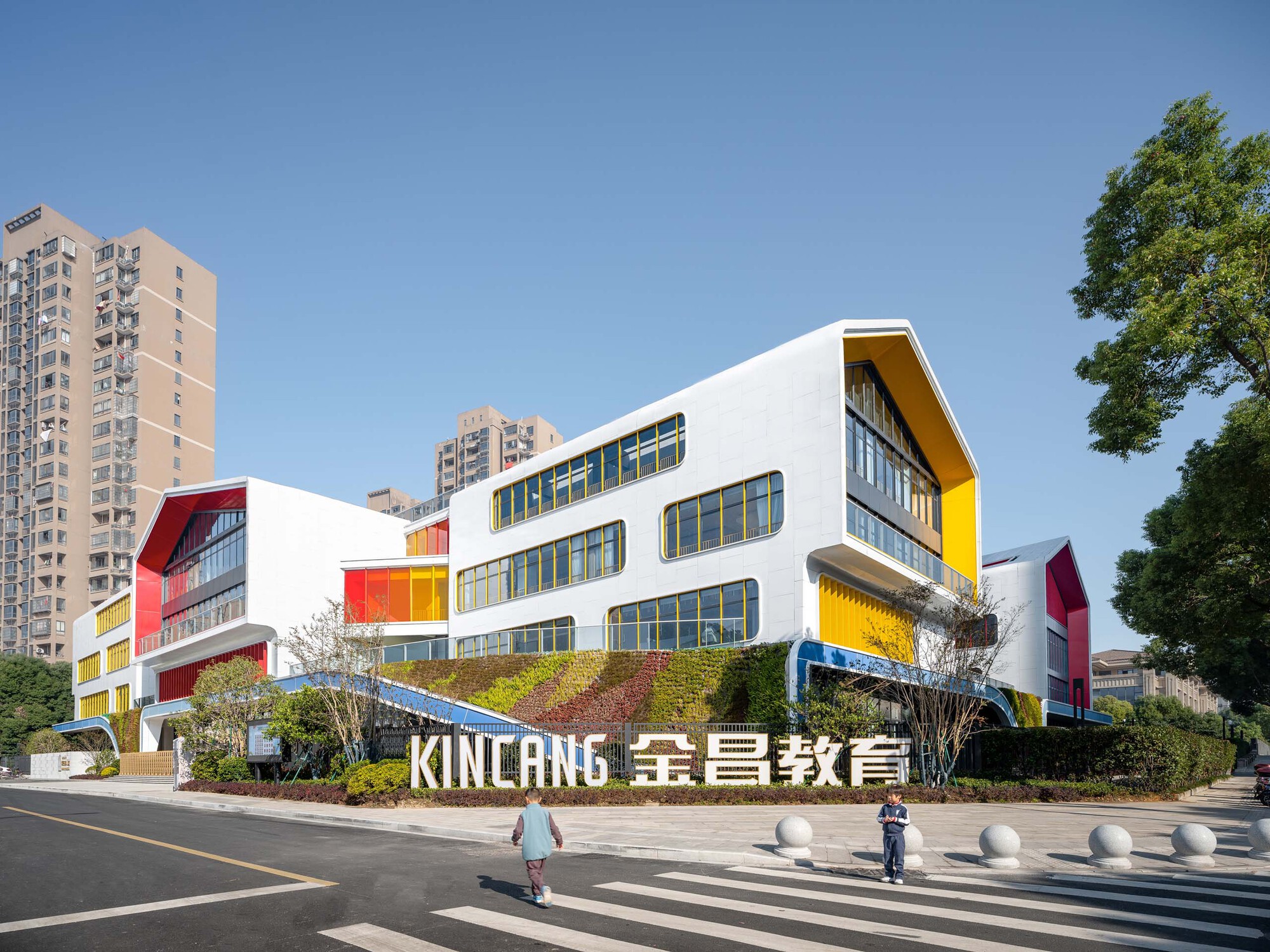Street view of the white facade with curved forms and colored panels against highrise residential towers
