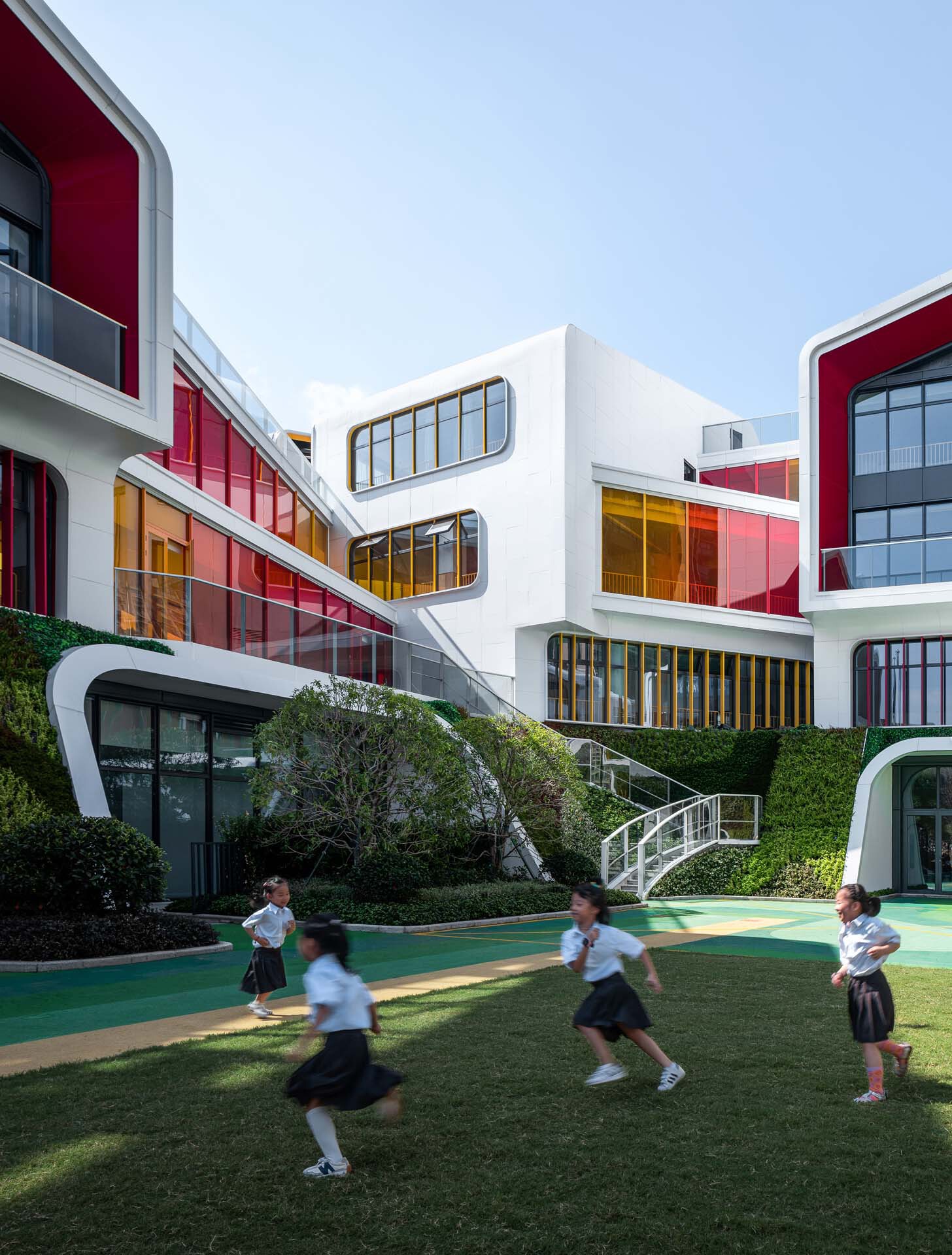Courtyard with green running track and children playing on lawn below terraced white volumes with glazed facades