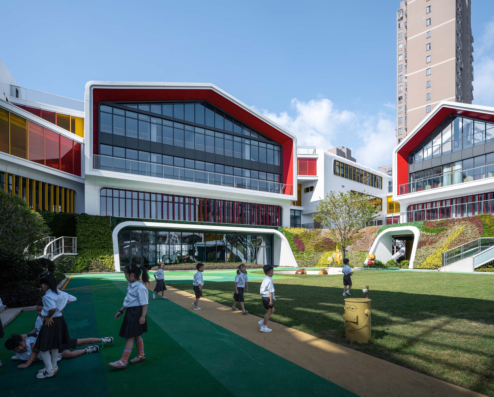 Schoolchildren gathered on the green play track beneath portal-like openings in the white building base