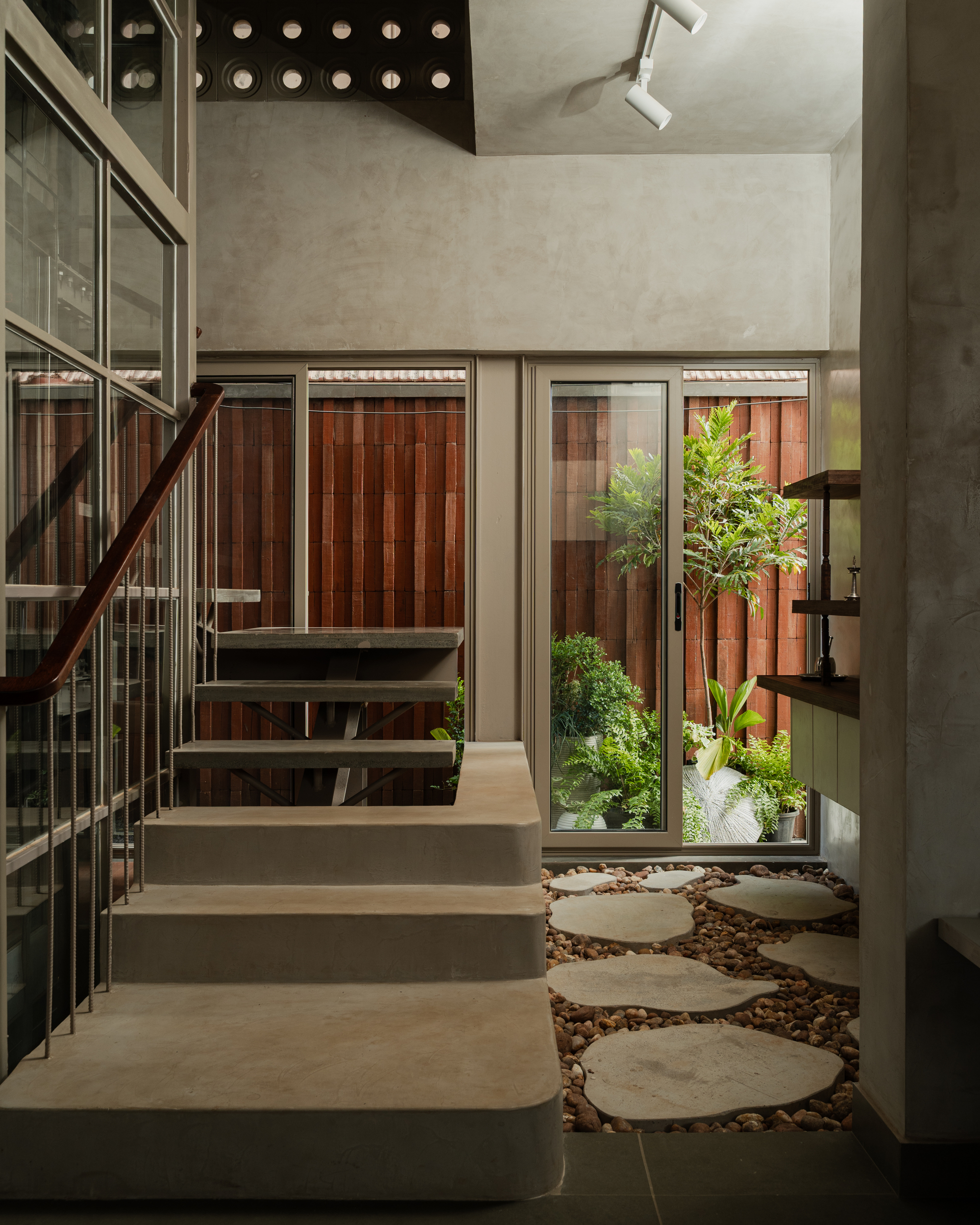 Interior stair with circular stepping stones in gravel courtyard and potted plants beside glass doors