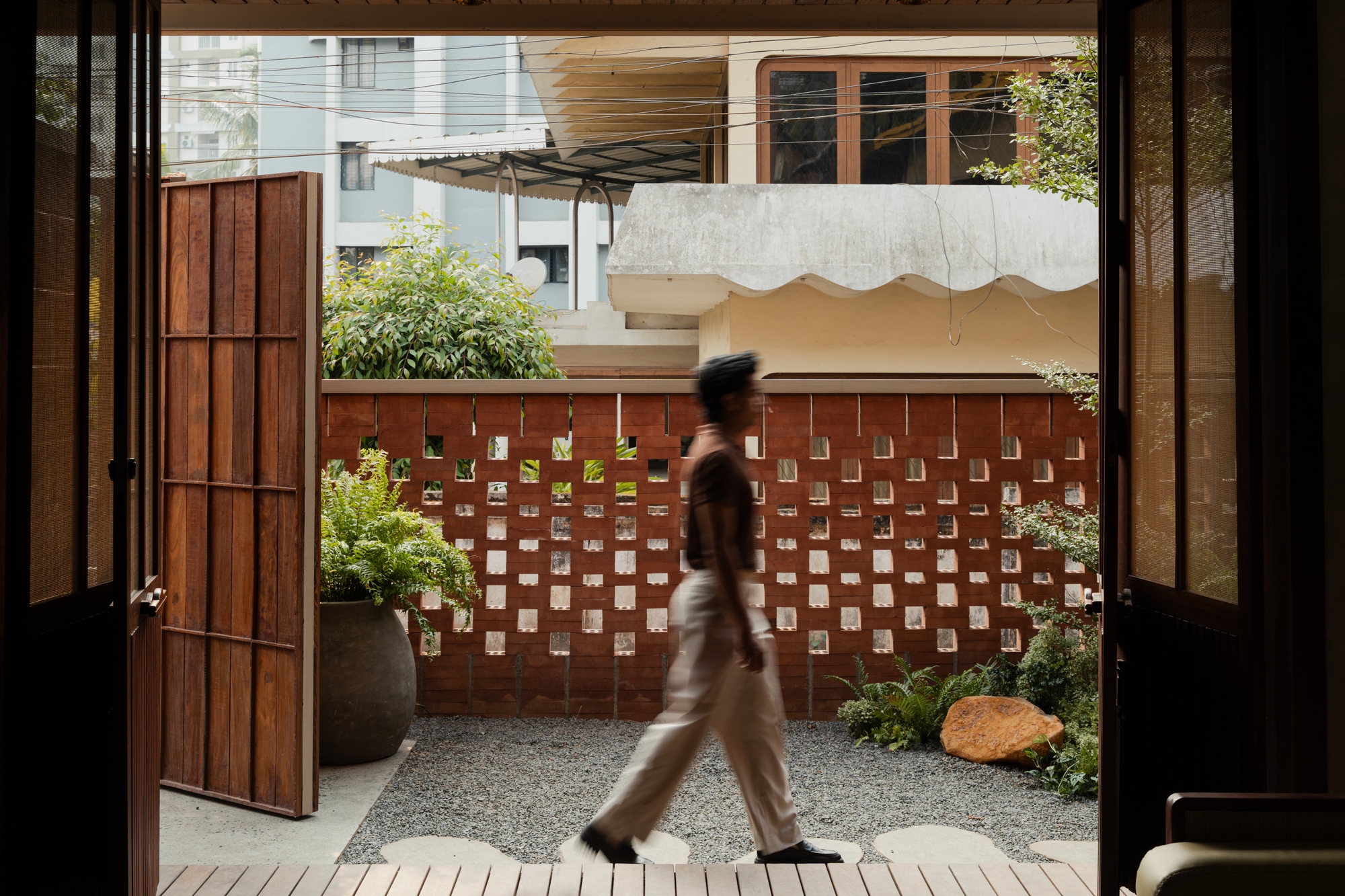 View through open doors to gravel courtyard with perforated brick wall and figure walking past