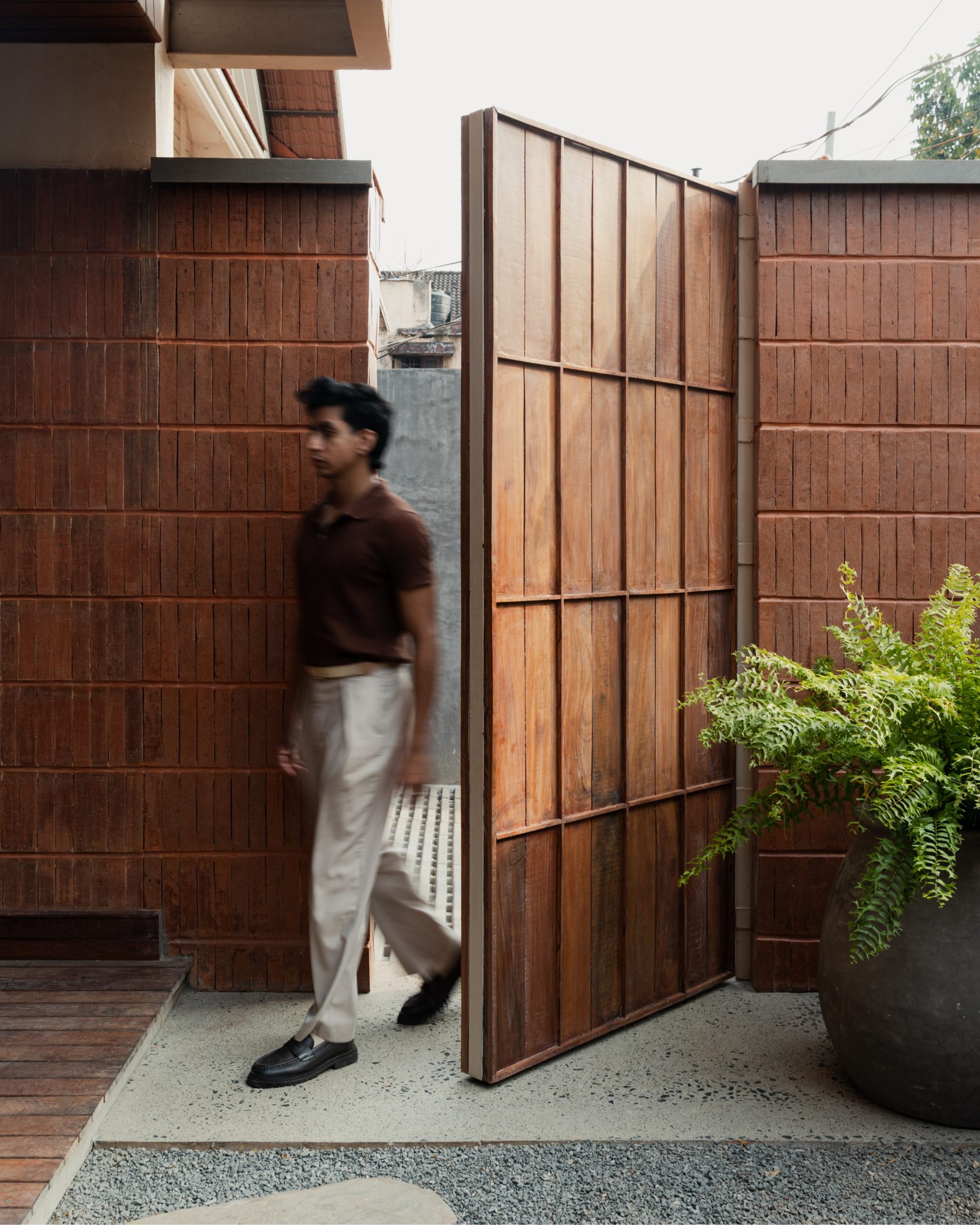 Pivoting timber screen with black metal frame beside tiled walls and a figure in motion