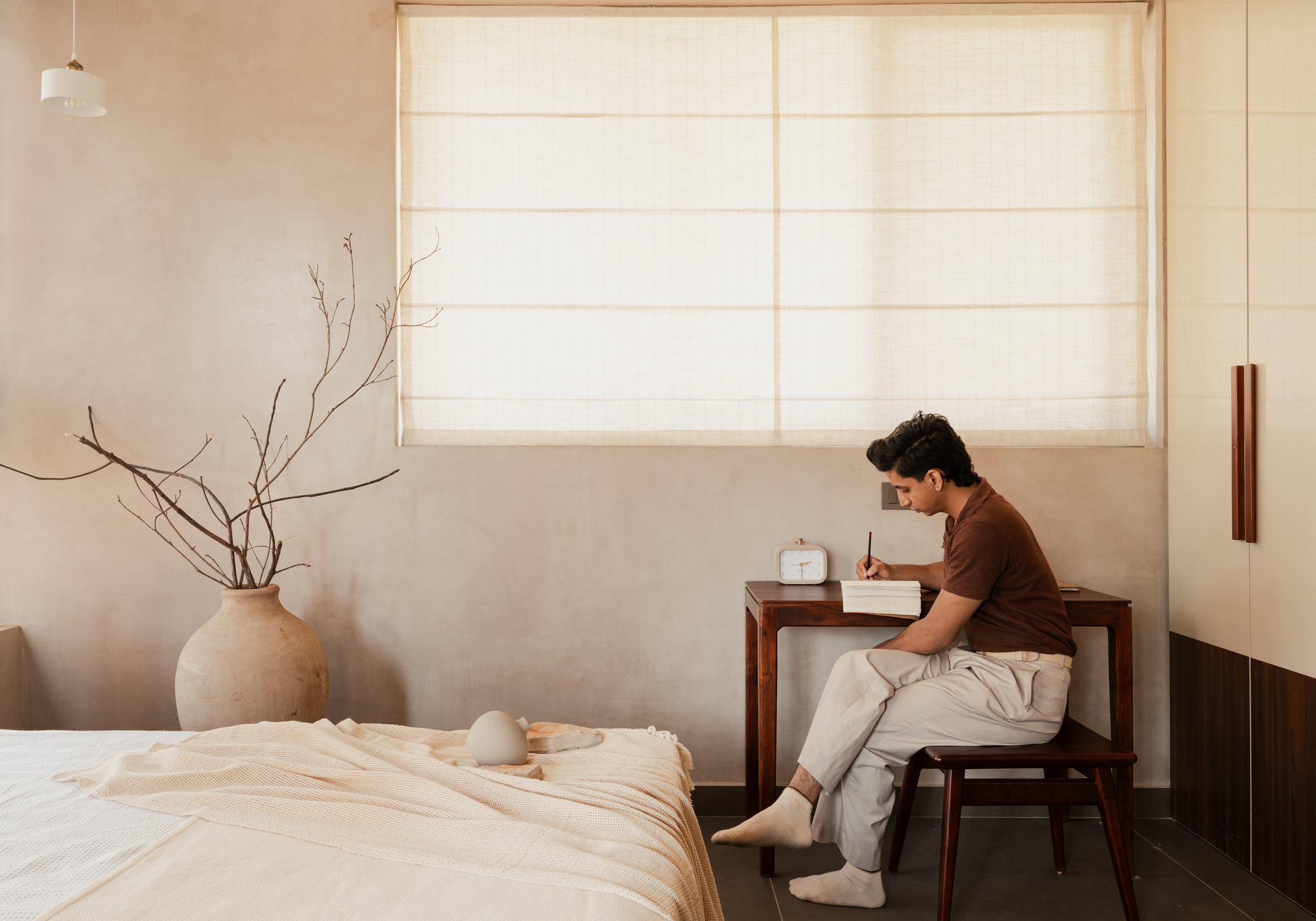 Bedroom workspace with person at writing desk beneath a translucent fabric roman shade
