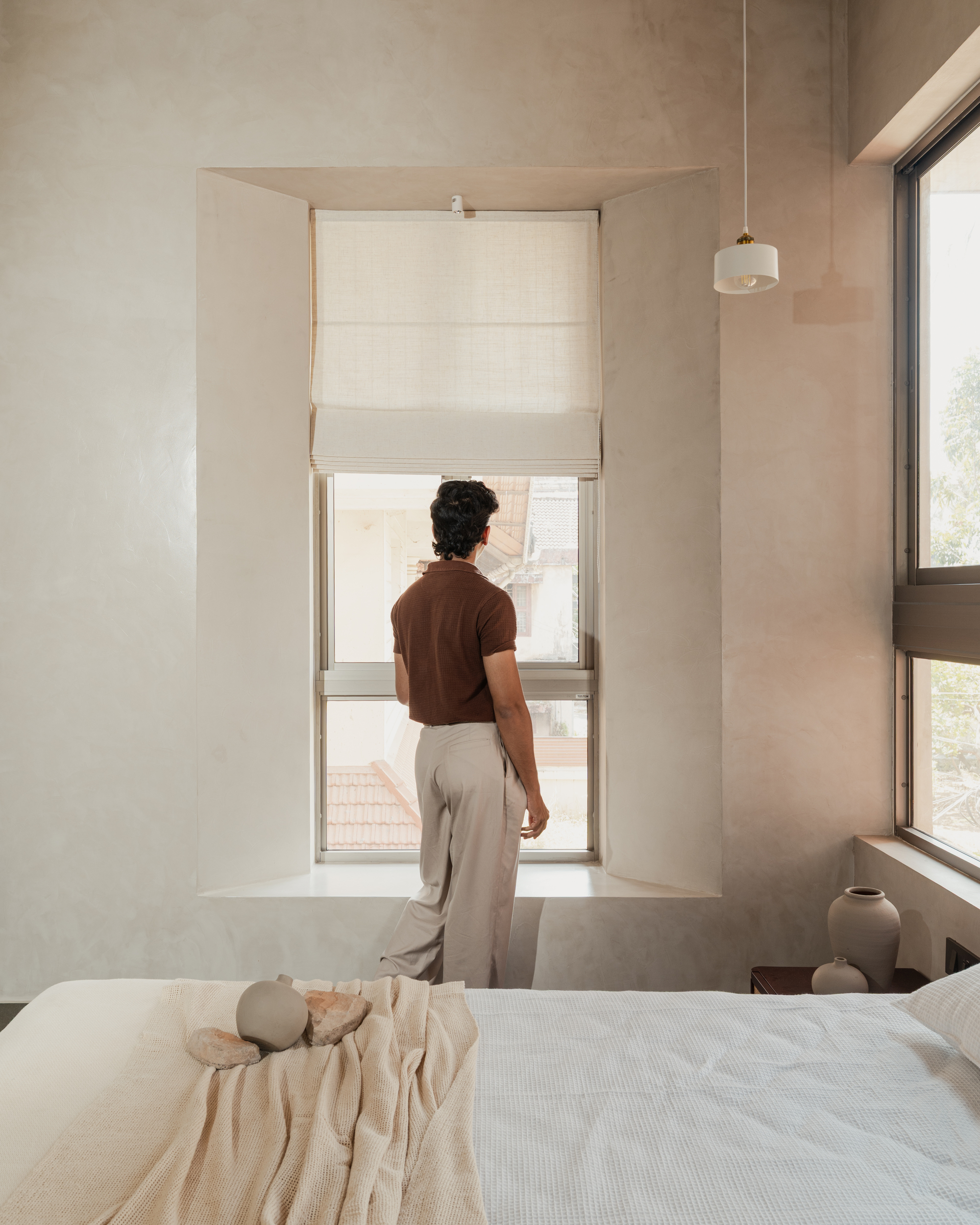 Tall recessed window niche with person looking out over bed and cream-toned plastered walls