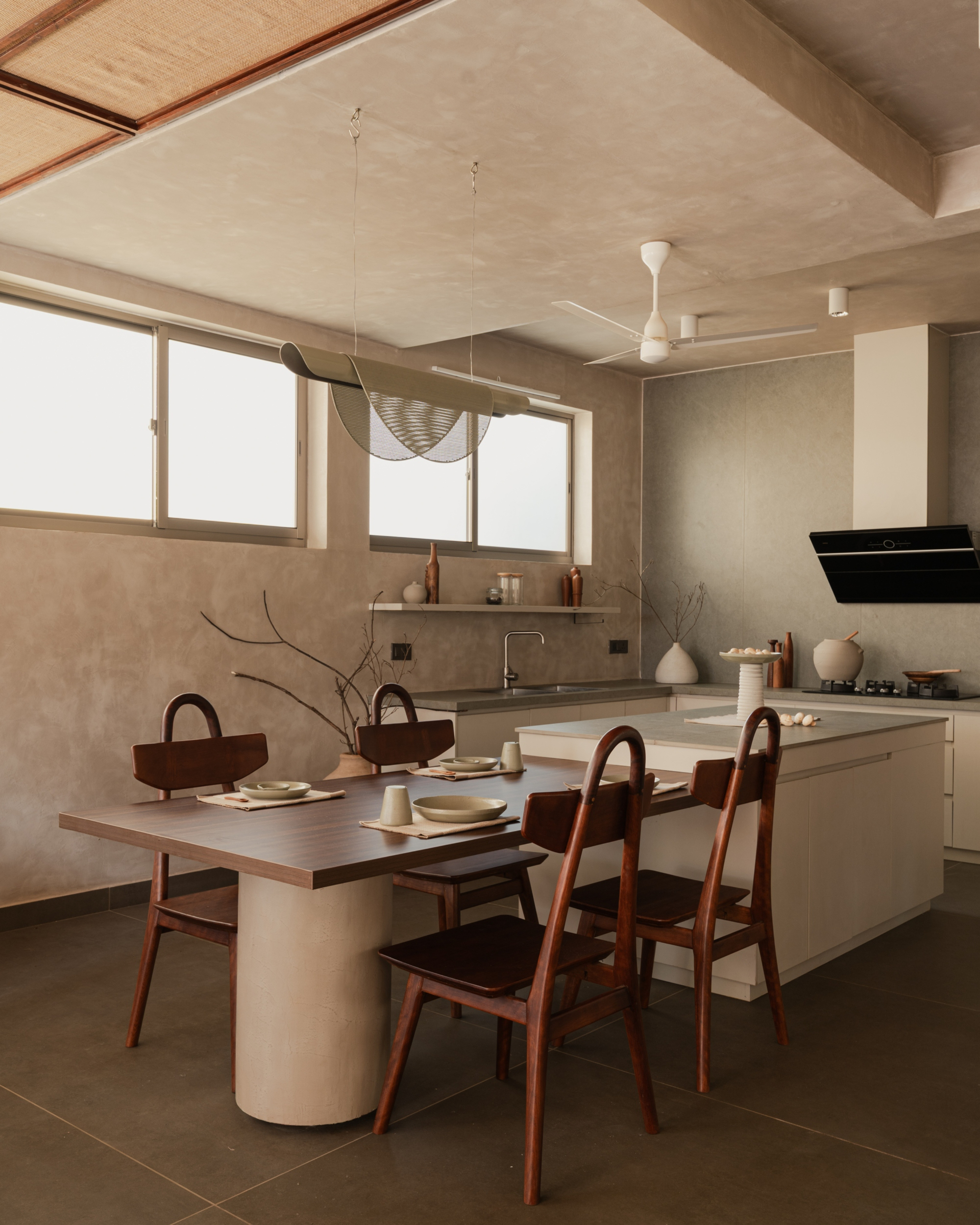 Open kitchen and dining area with cylindrical plaster table base beneath sliding frosted glass windows