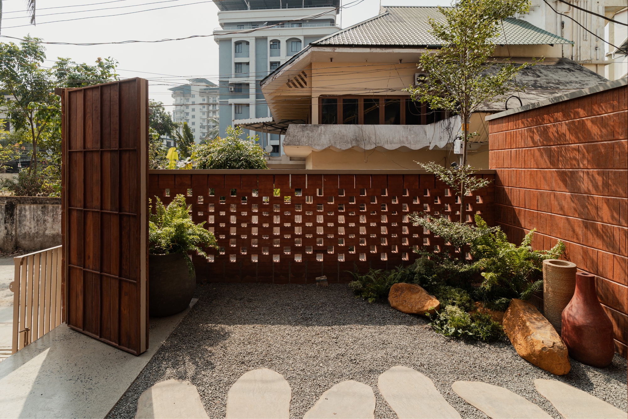 Courtyard garden with perforated terracotta screen wall and gravel flooring surrounded by timber cladding and planters