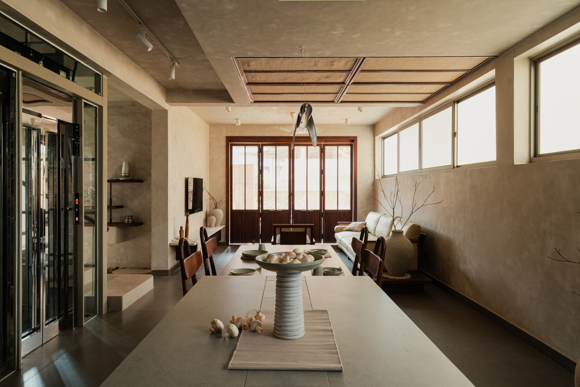 Living and dining space with timber slatted ceiling panel and dark wood partition screens under concrete soffit