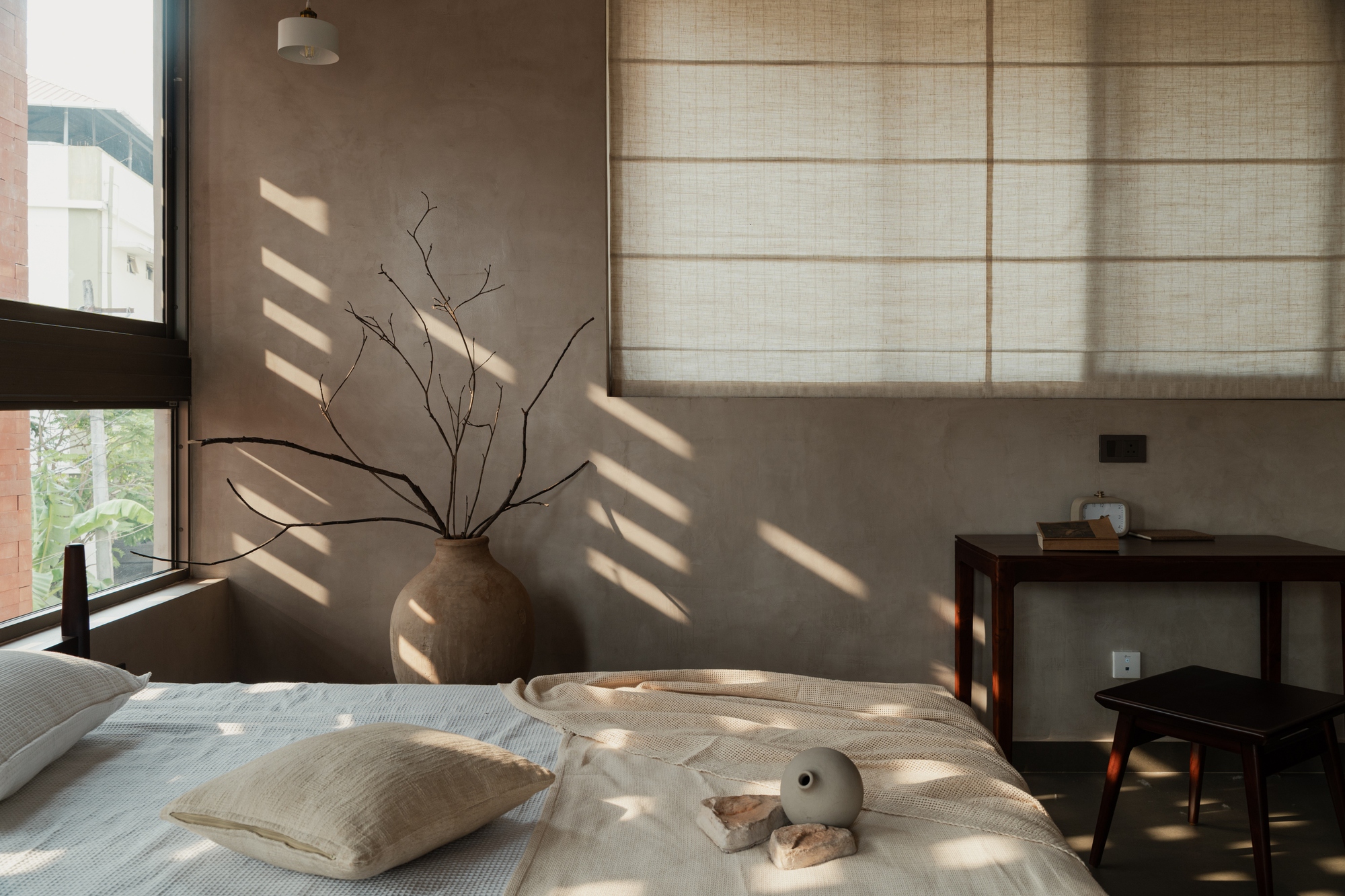 Low-angle view of the bed corner with sunlight patterns from the perforated brick facade