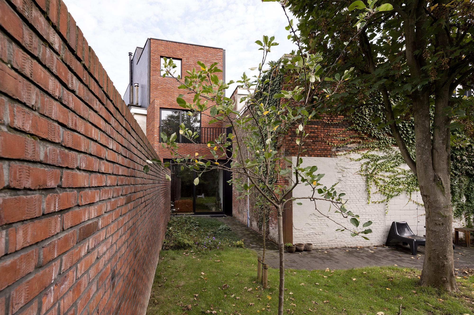 Rear garden courtyard with red brick walls, young trees and a painted white adjoining structure