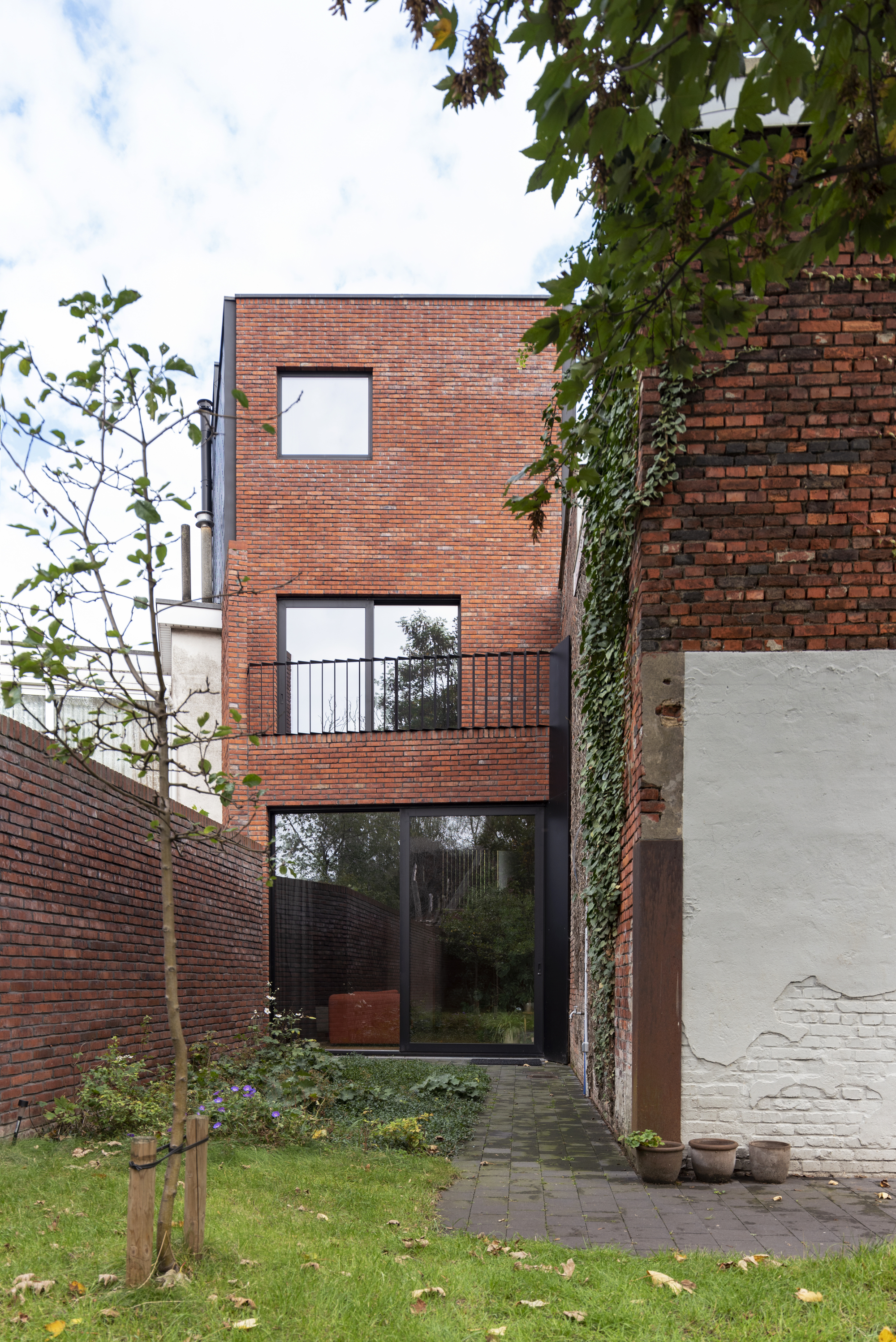 Narrow brick facade with stacked windows and a glass door opening to a planted garden