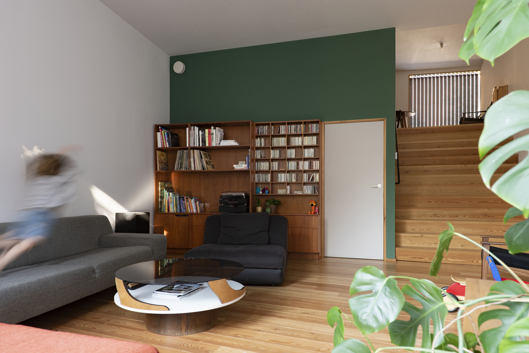 Living room with a dark green accent wall, timber bookshelves and a person in motion