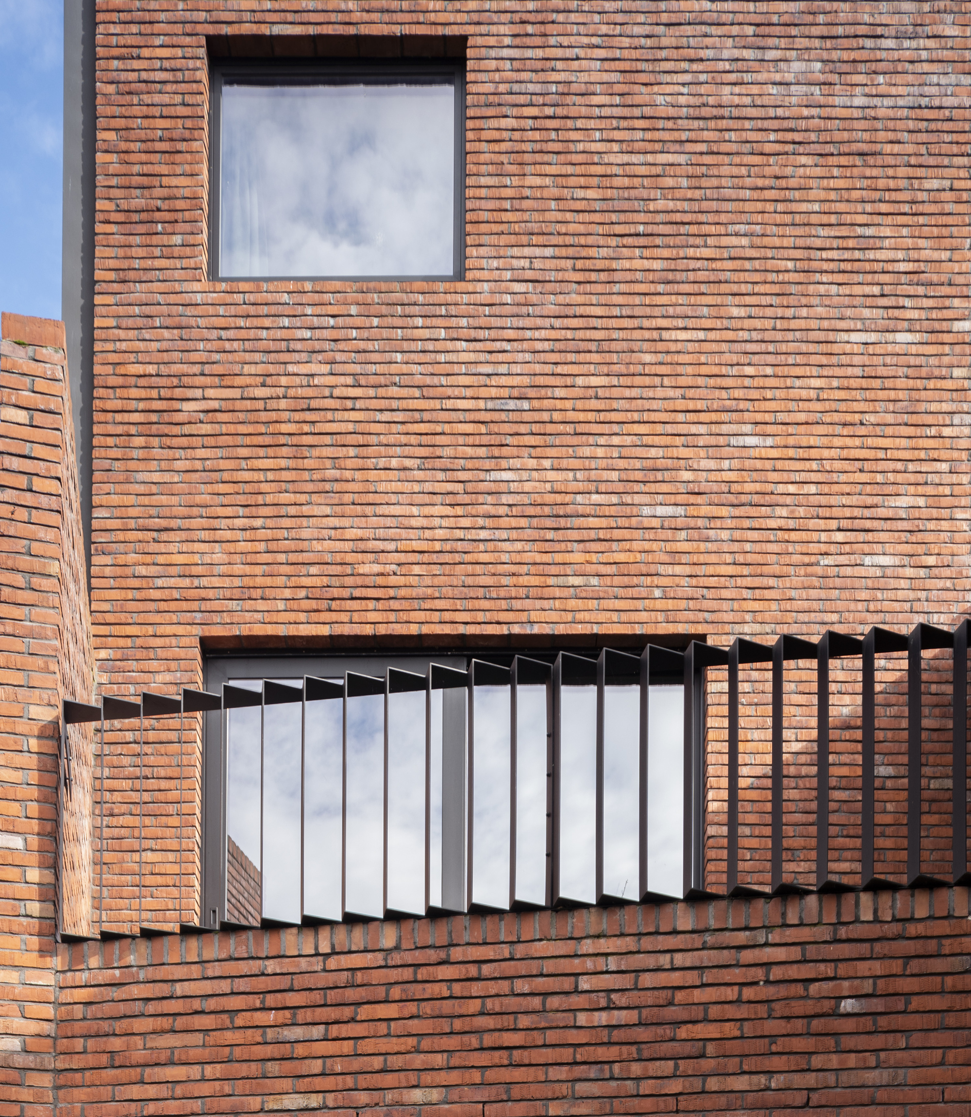 Orange brick facade with folding white metal louvers framing a recessed balcony opening