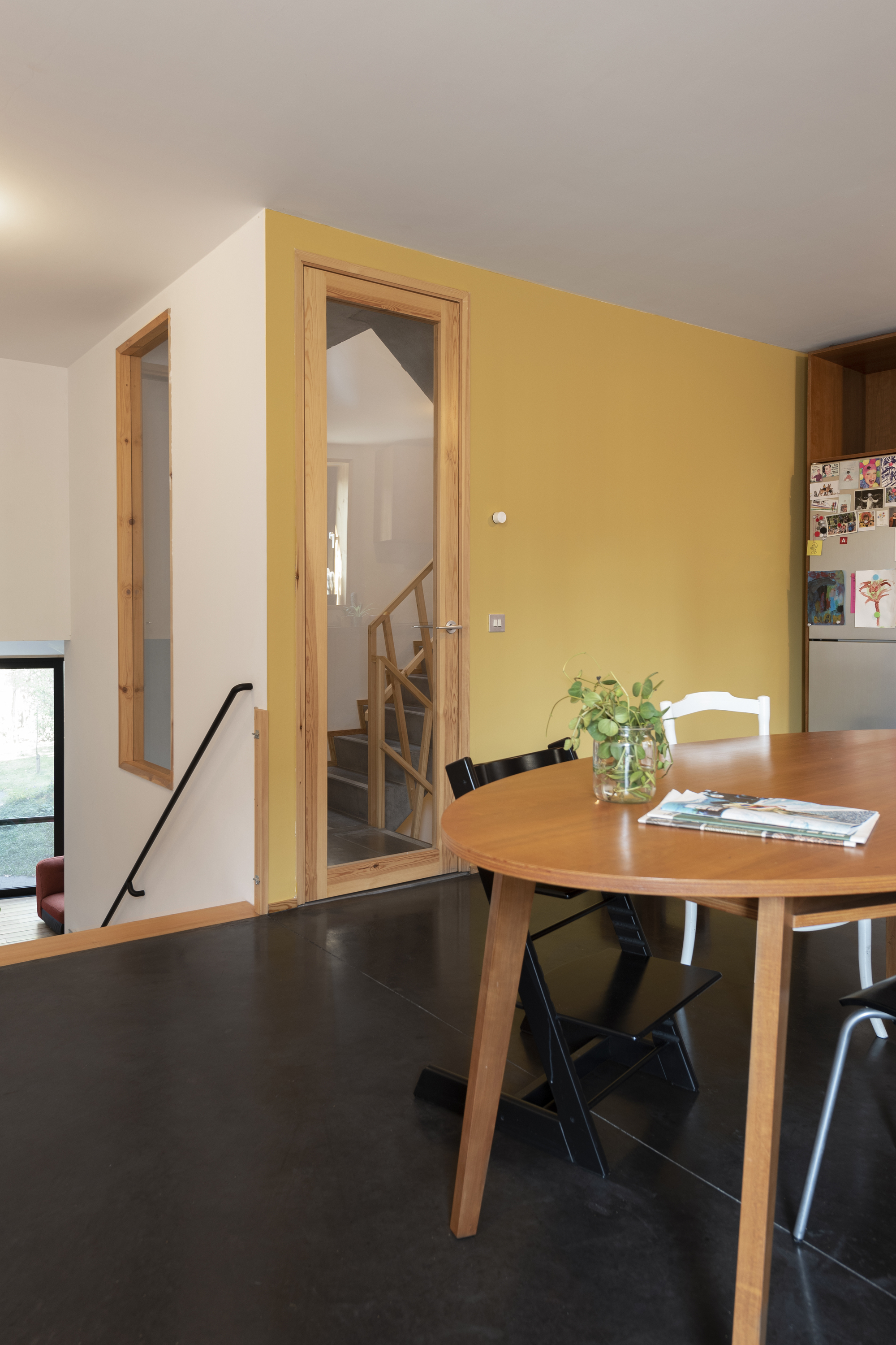 Dining area with timber doorway framing view to staircase and yellow accent wall
