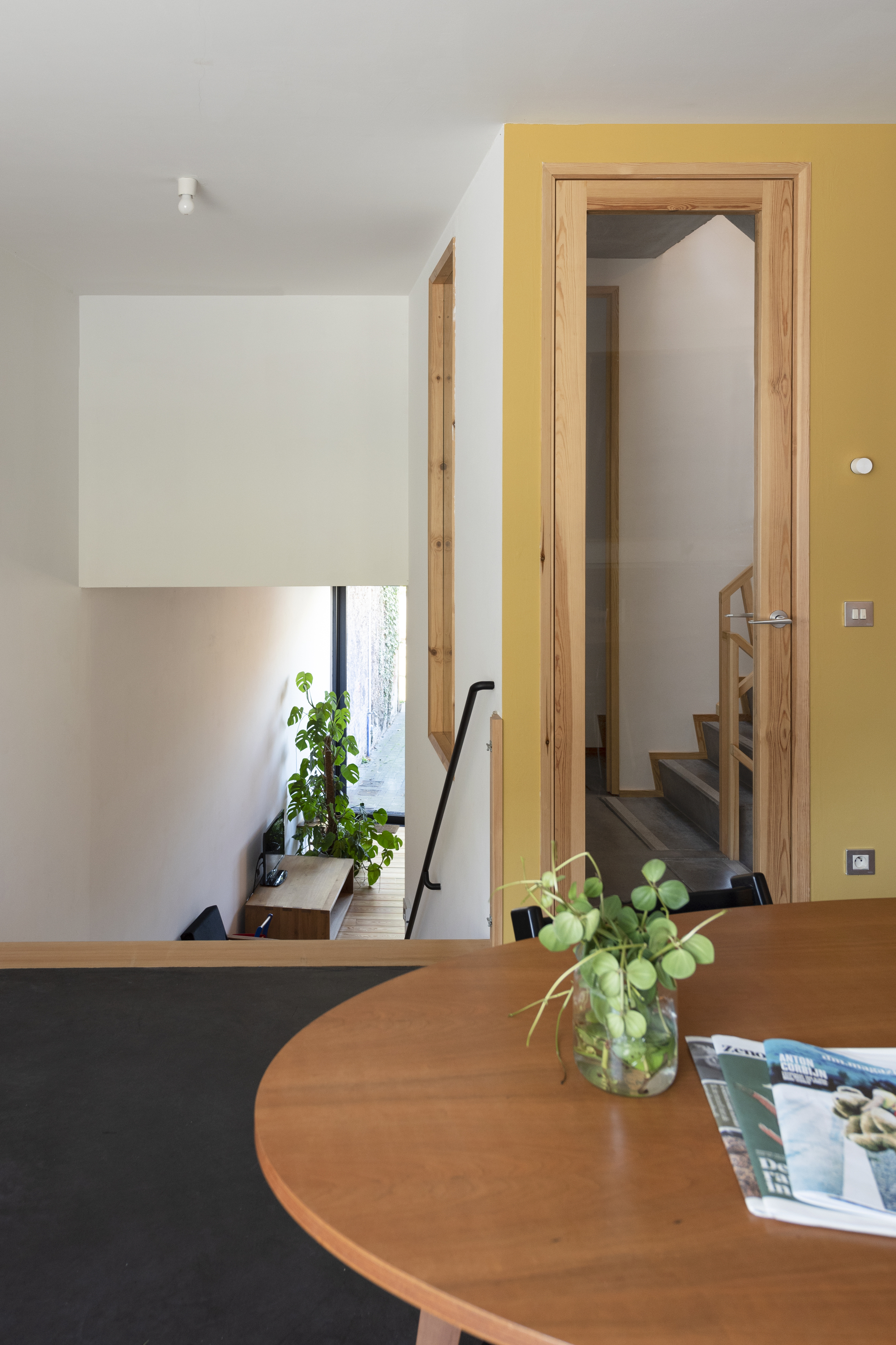 Round timber dining table with view through doorway to planted stairwell below