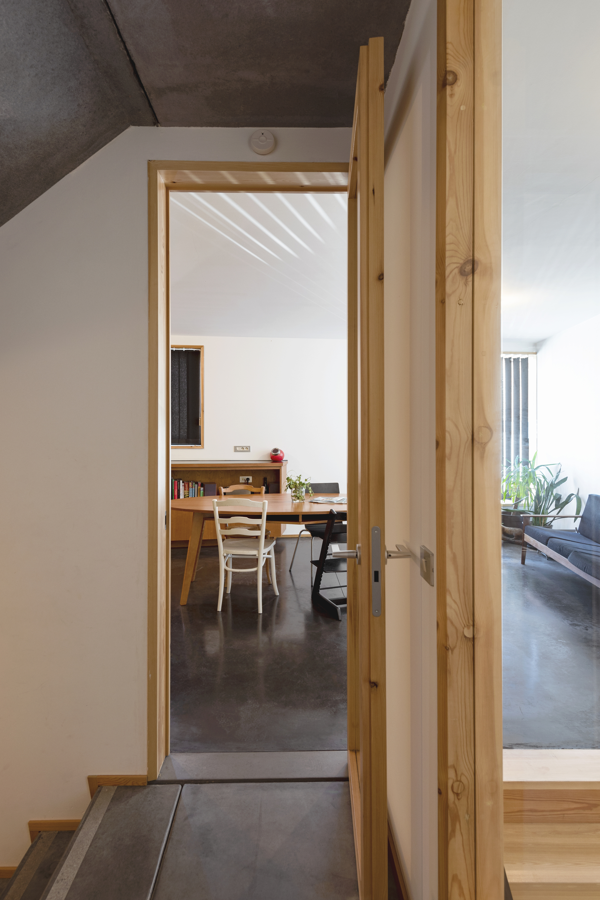 Timber-framed doorway opening from corridor to dining room with dark concrete flooring